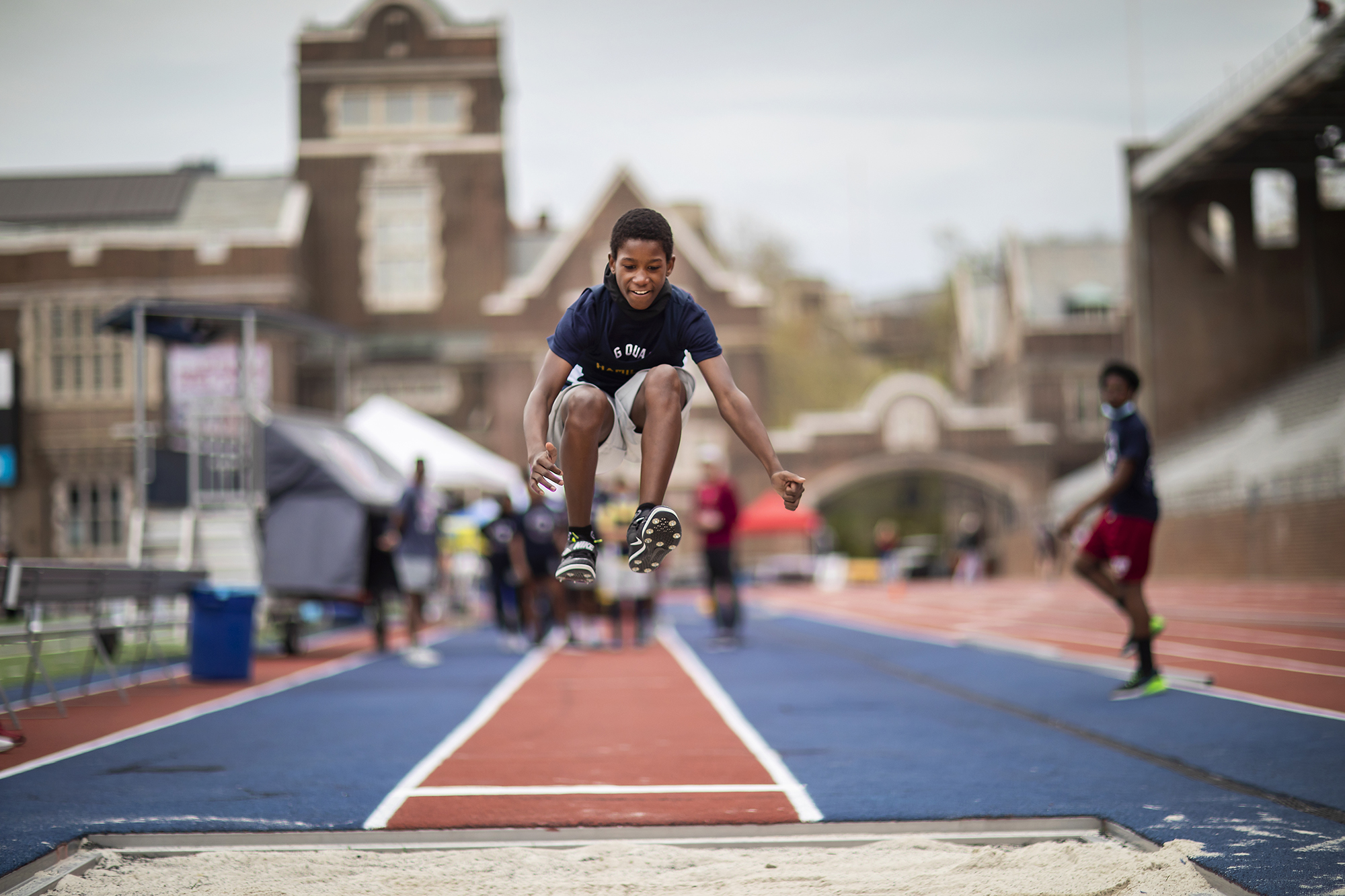 A student is airborne, in the midst of his long jump