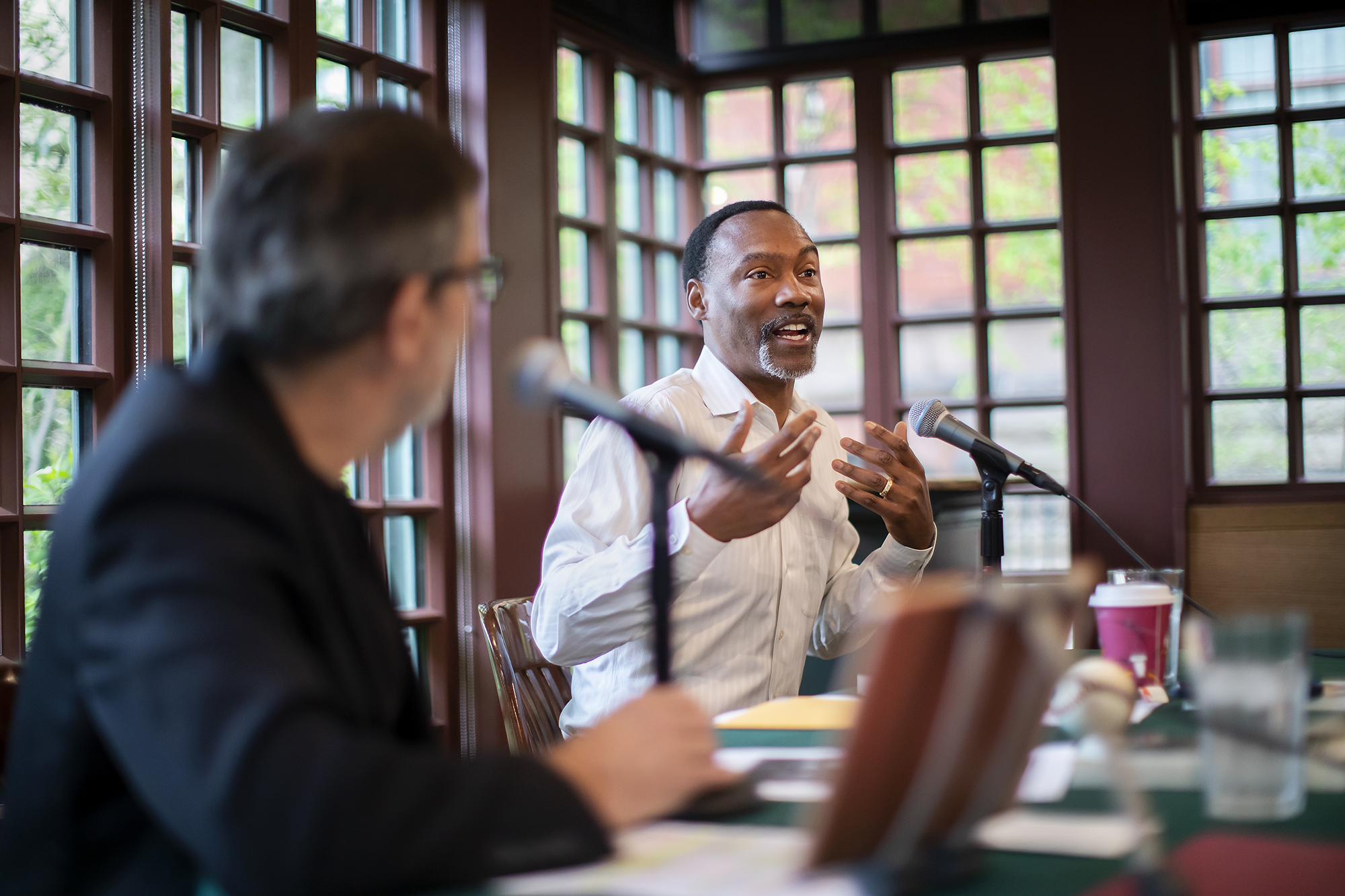 Doug Glanville sitting at table speaking at microphone gesturing with his hands