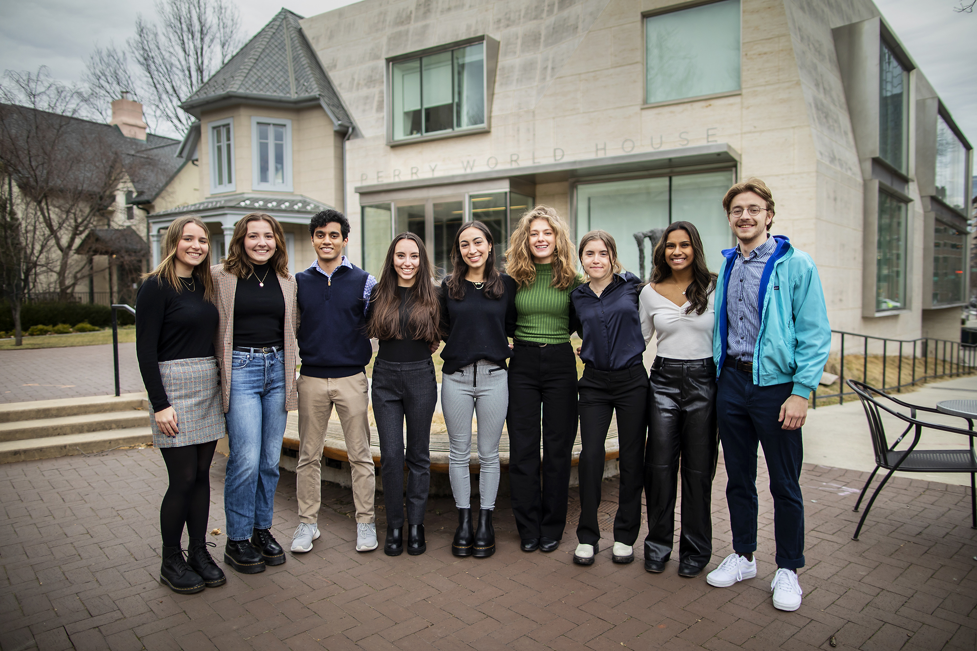 Group of students face camera, arm in arm, in front of Perry World House