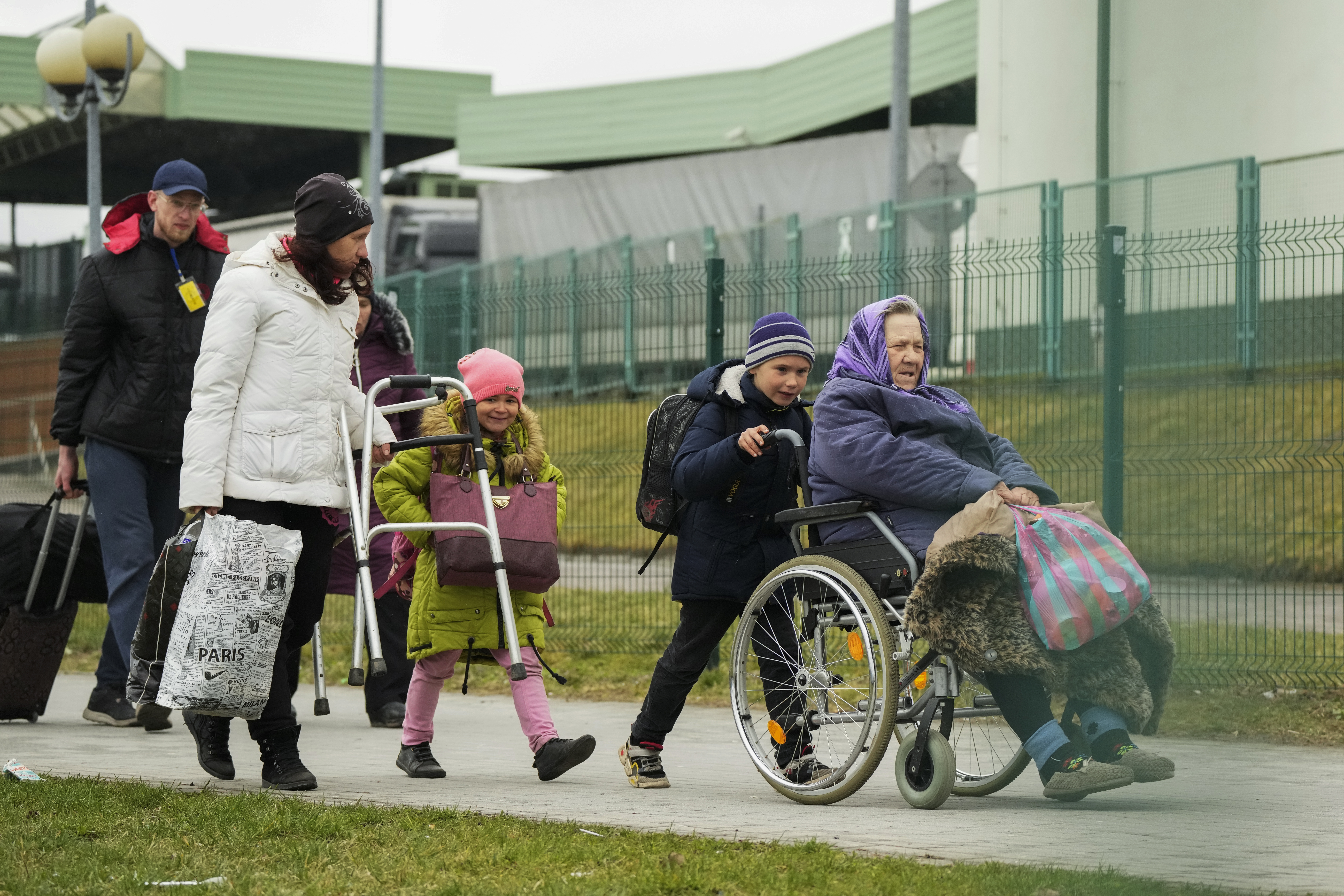 Ukrainian refugees including a woman in a wheelchair being pushed by a little boy, flee Ukraine into Poland