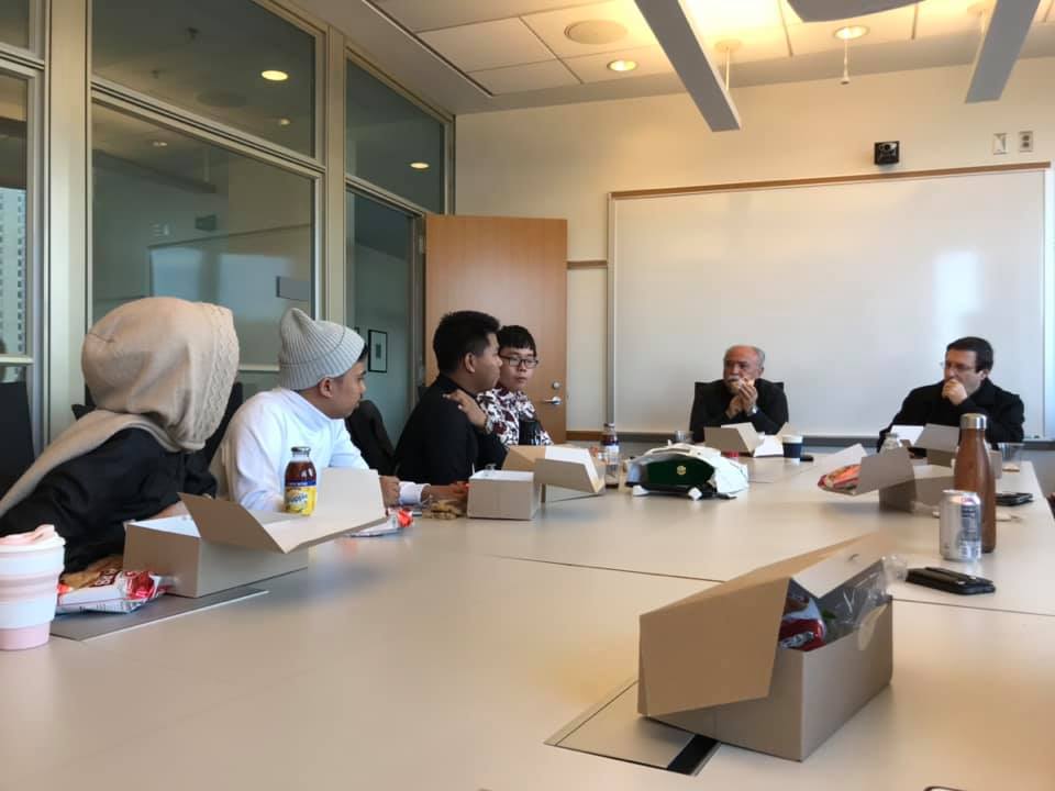 Students and teachers sitting in a conference room at a large table having a discussion. 