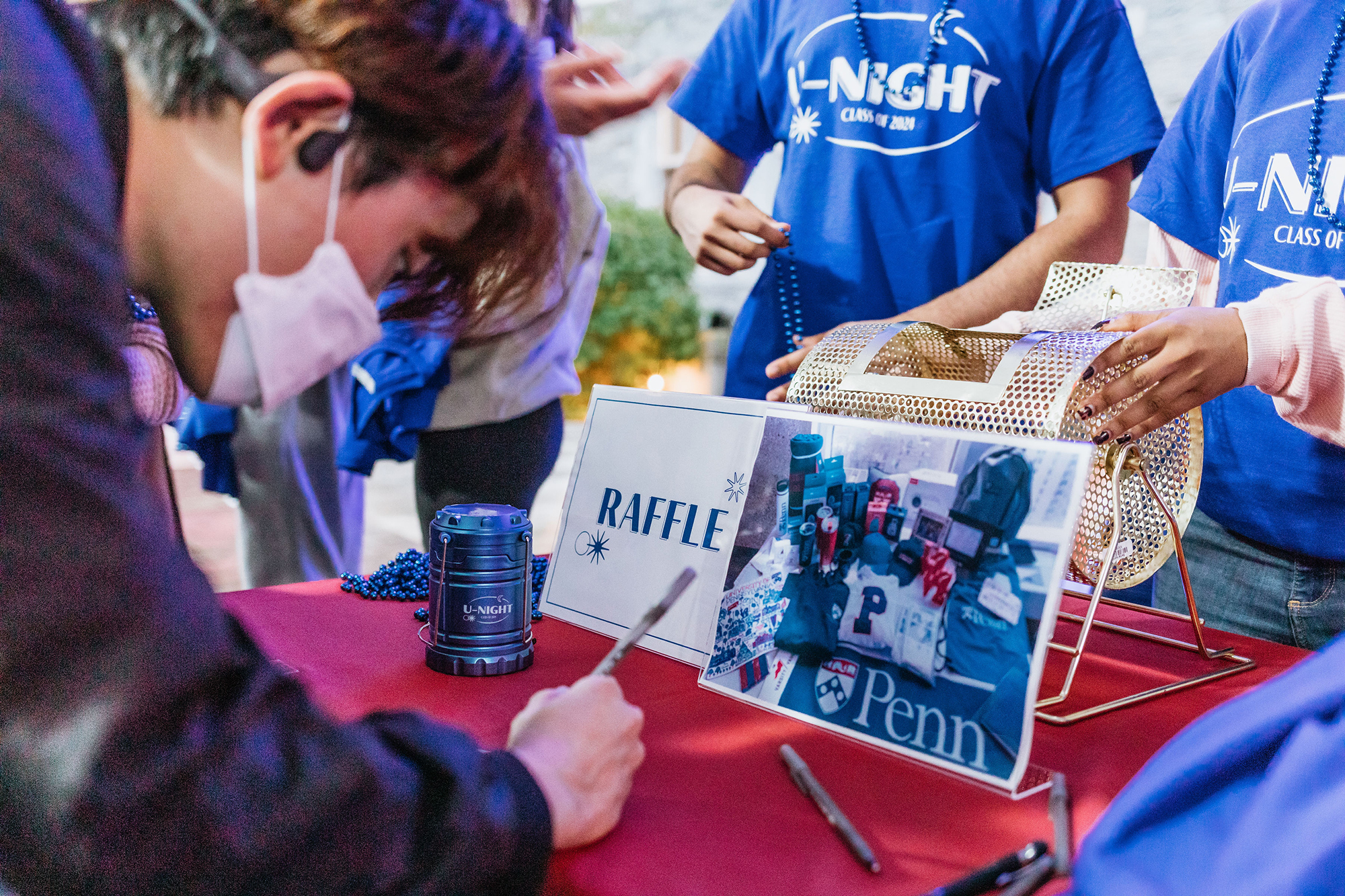 A masked student fills out a raffle ticket at a table under the tent at U-Night.