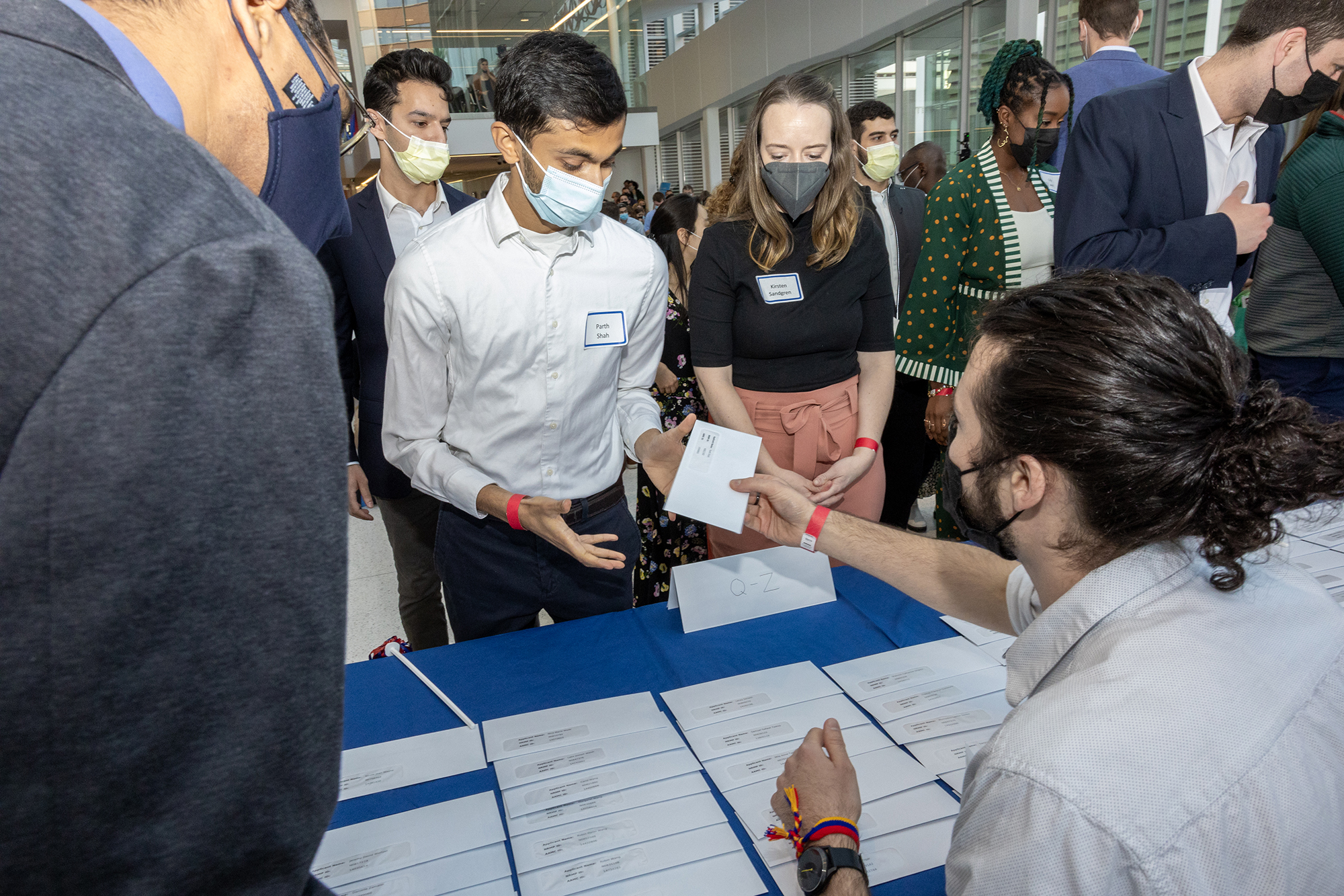 A Penn Med student receives their Match Day letter from someone seated at a table full of envelopes.
