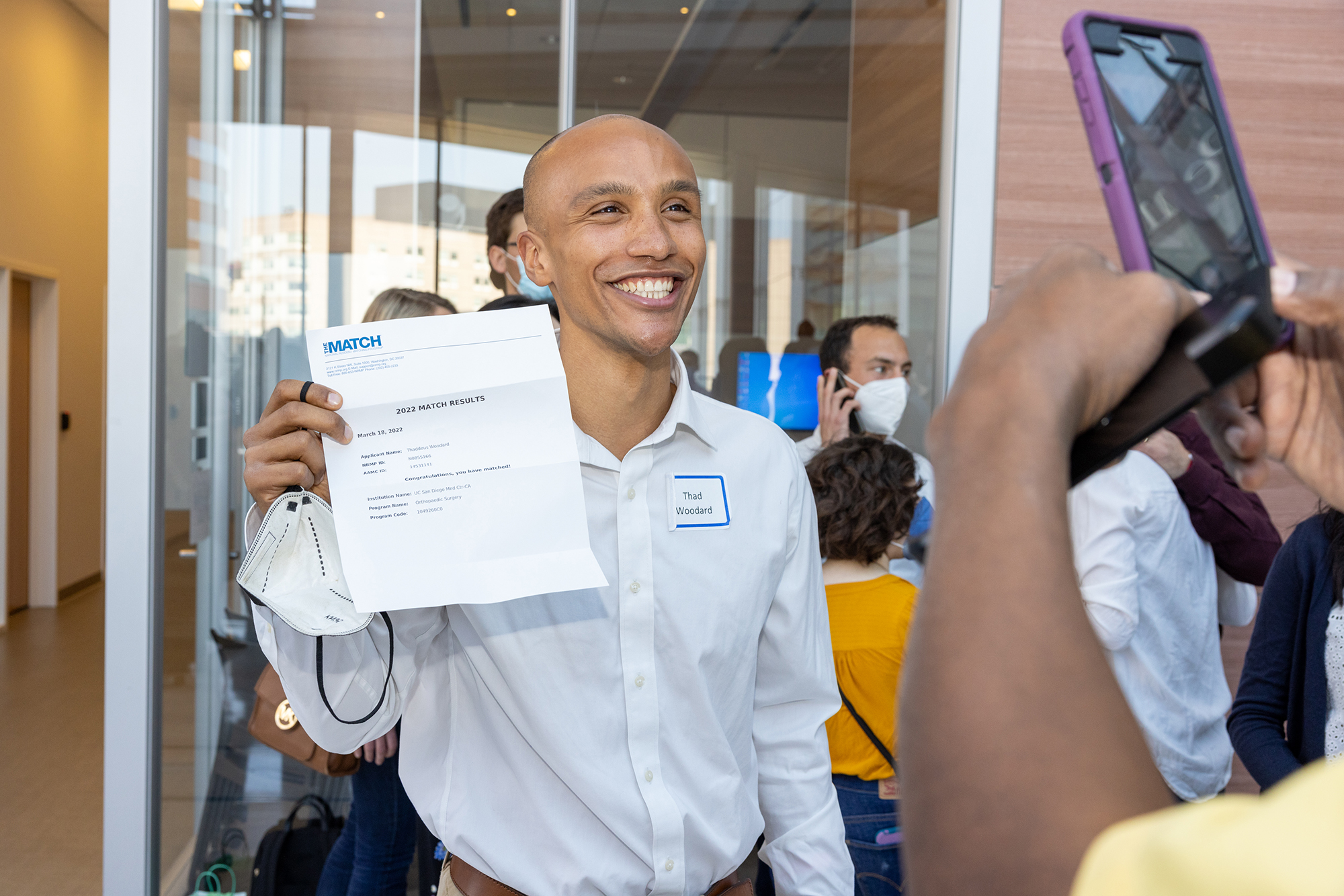 Penn Med student Theo Woodard smiles while holding up their Match Day letter.