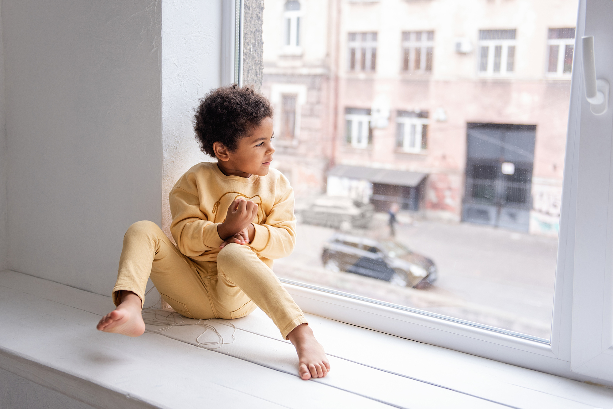 Young child looking out the window of an apartment building.