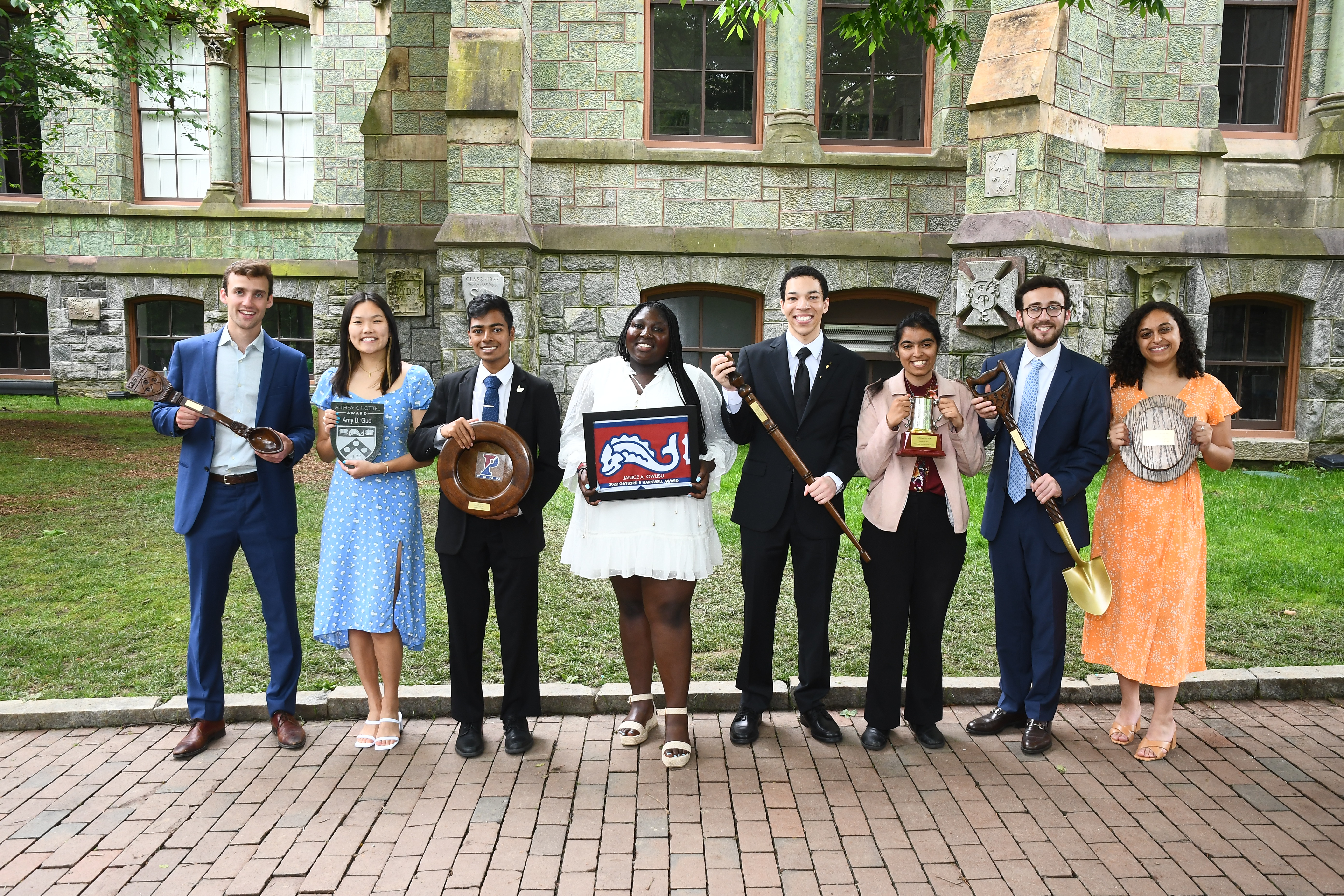 Eight students pose on Locust Walk with plaques and shovels