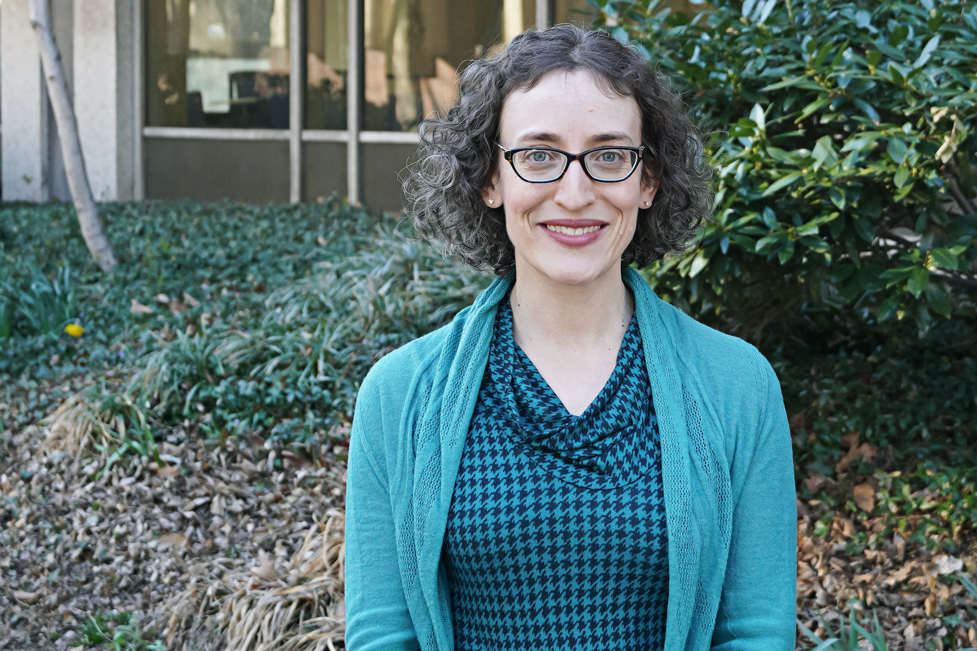 Rebecca Mendelson poses outside the library in front of green bushes