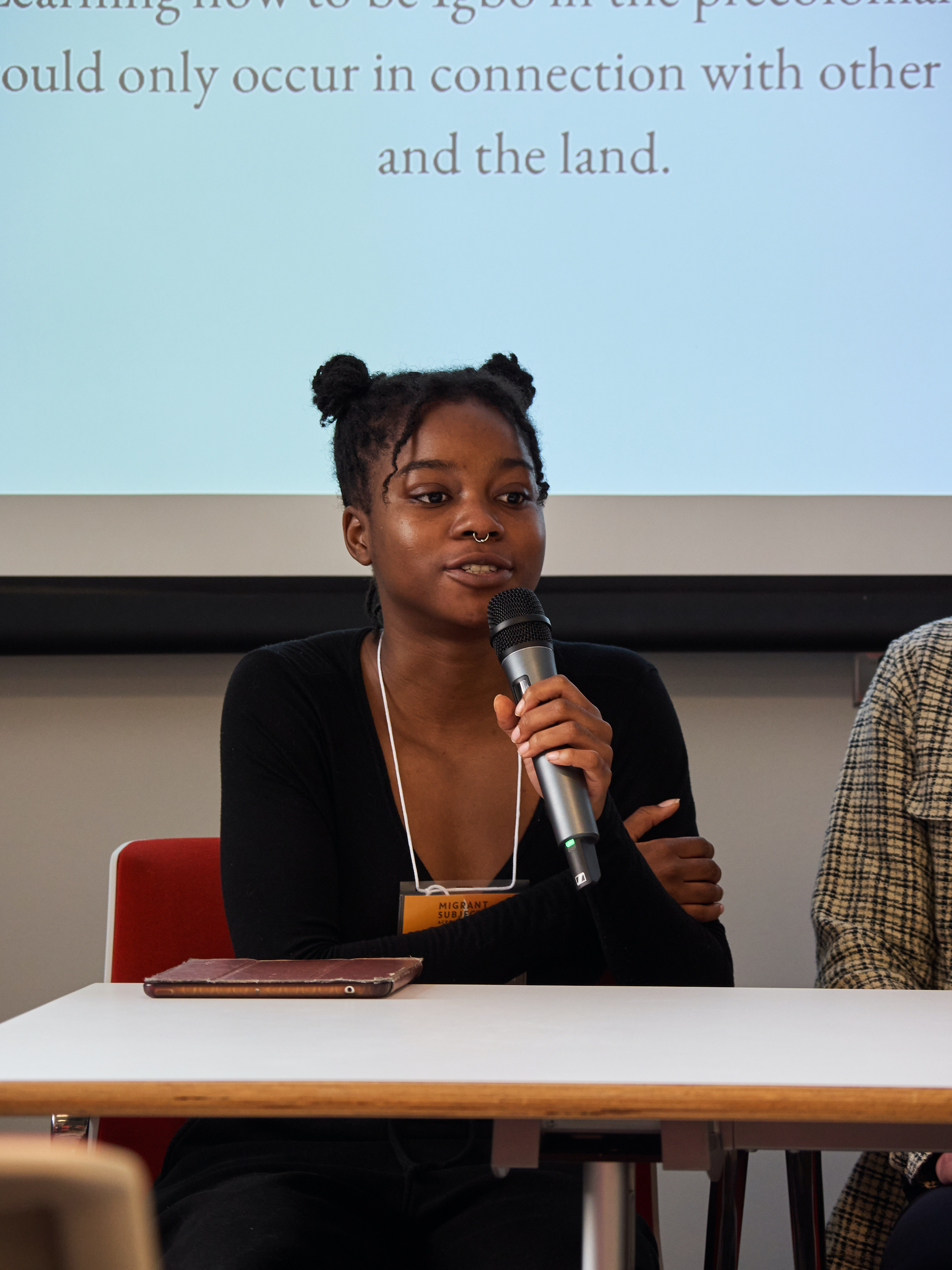 A woman speaks into a mic; the screen behind her reads, "could only occur in connection with each other and the land"
