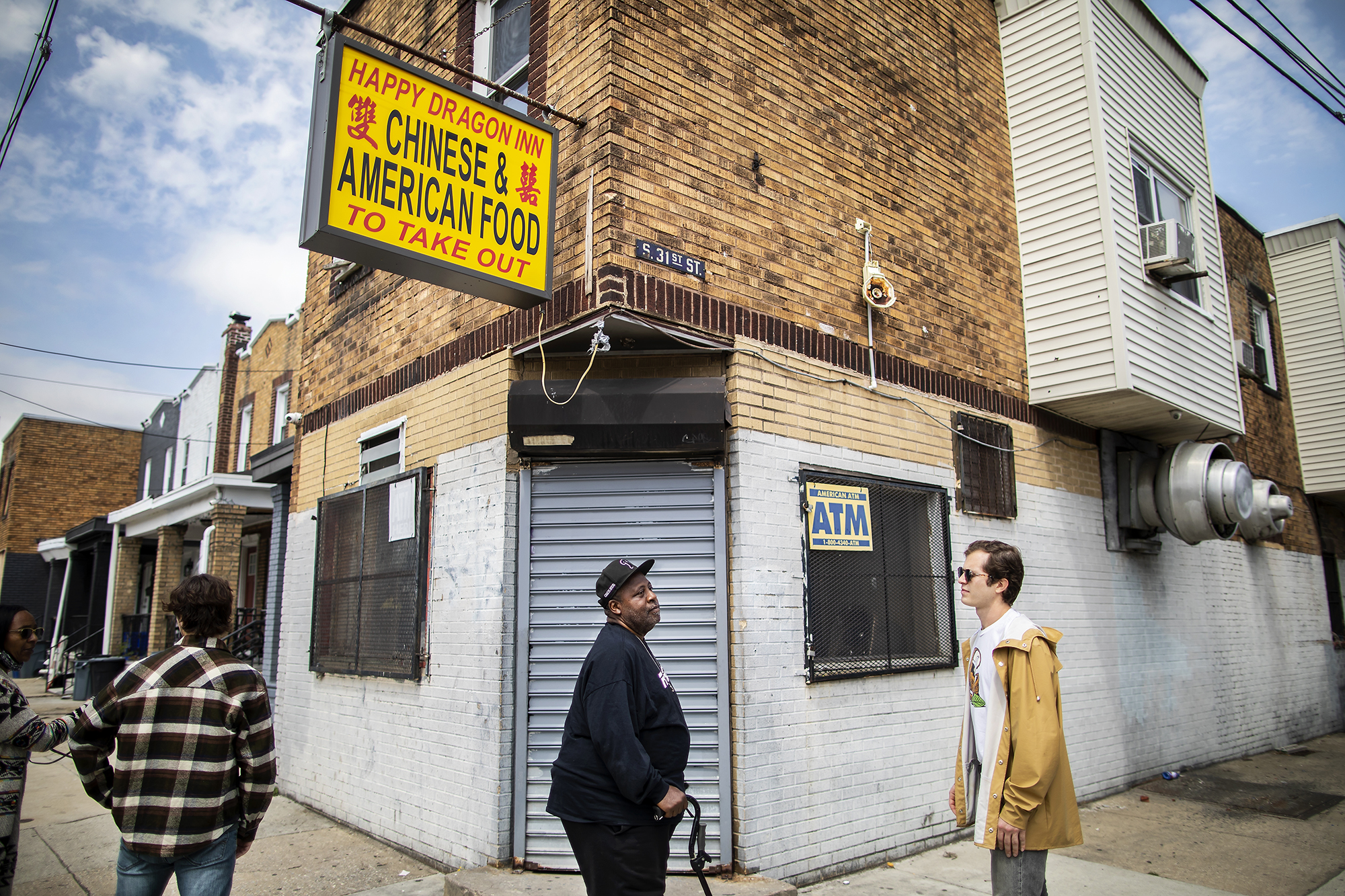 Tammy Reeves, Eli Moraru, Charles Reeves, and Alexandre Imbot stand at the corner of a brick building. A yellow sign reads: Happy Dragon Inn Chinese & American food to take out.