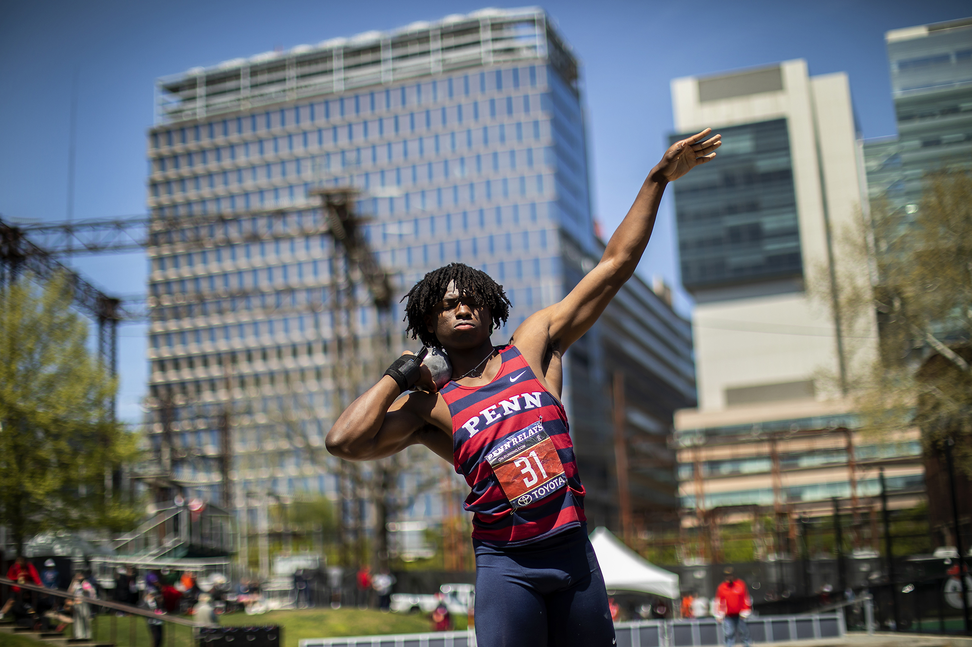 An athlete in a Penn jersey about to throw a shot put.