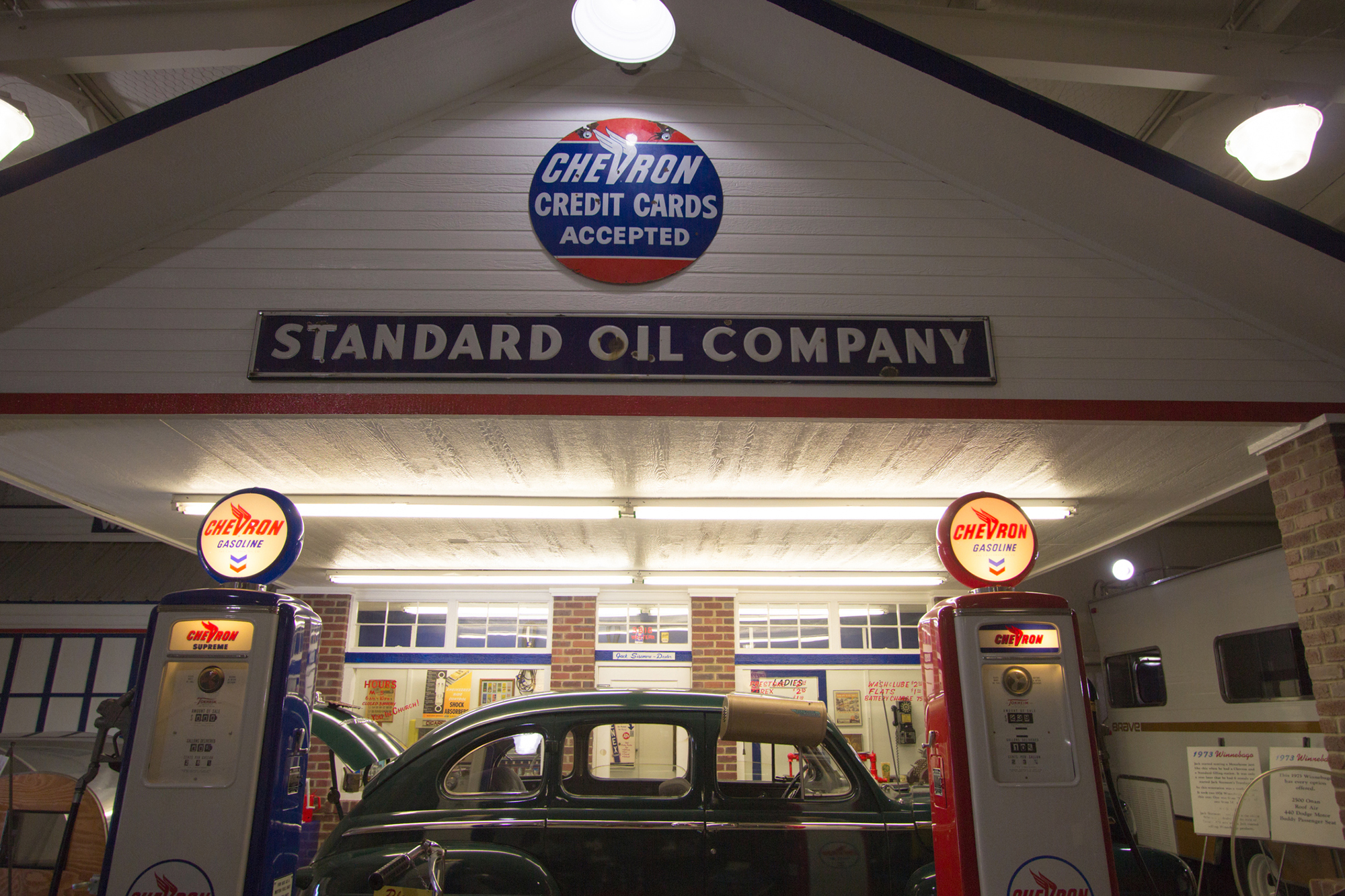 Car parked between pumps at a gas station in the 1970s beneath a sign reading STANDARD OIL COMPANY.
