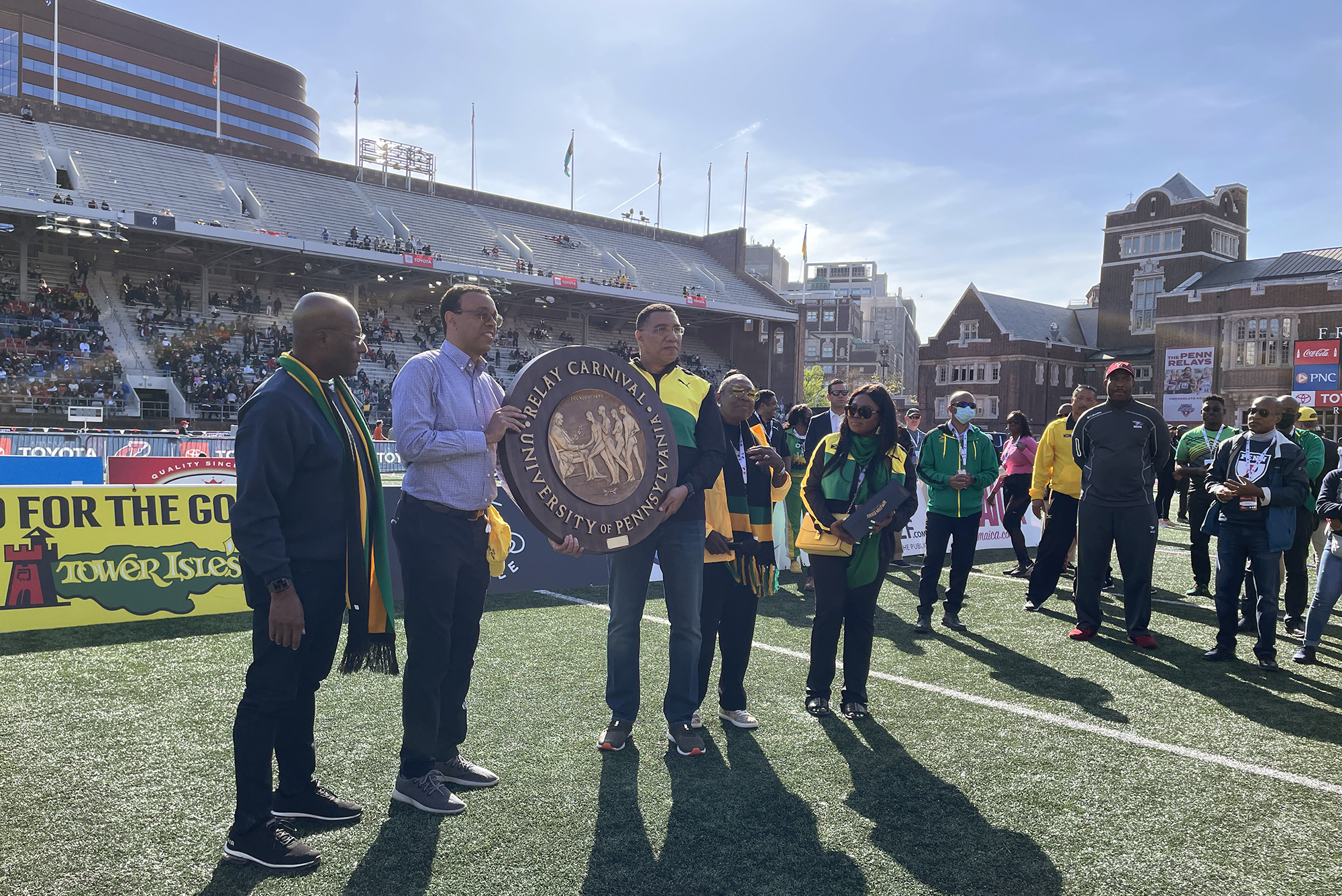 Wendell Pritchett on Franklin Field holding a large Penn Relays seal with the prime minister of Jamaica.
