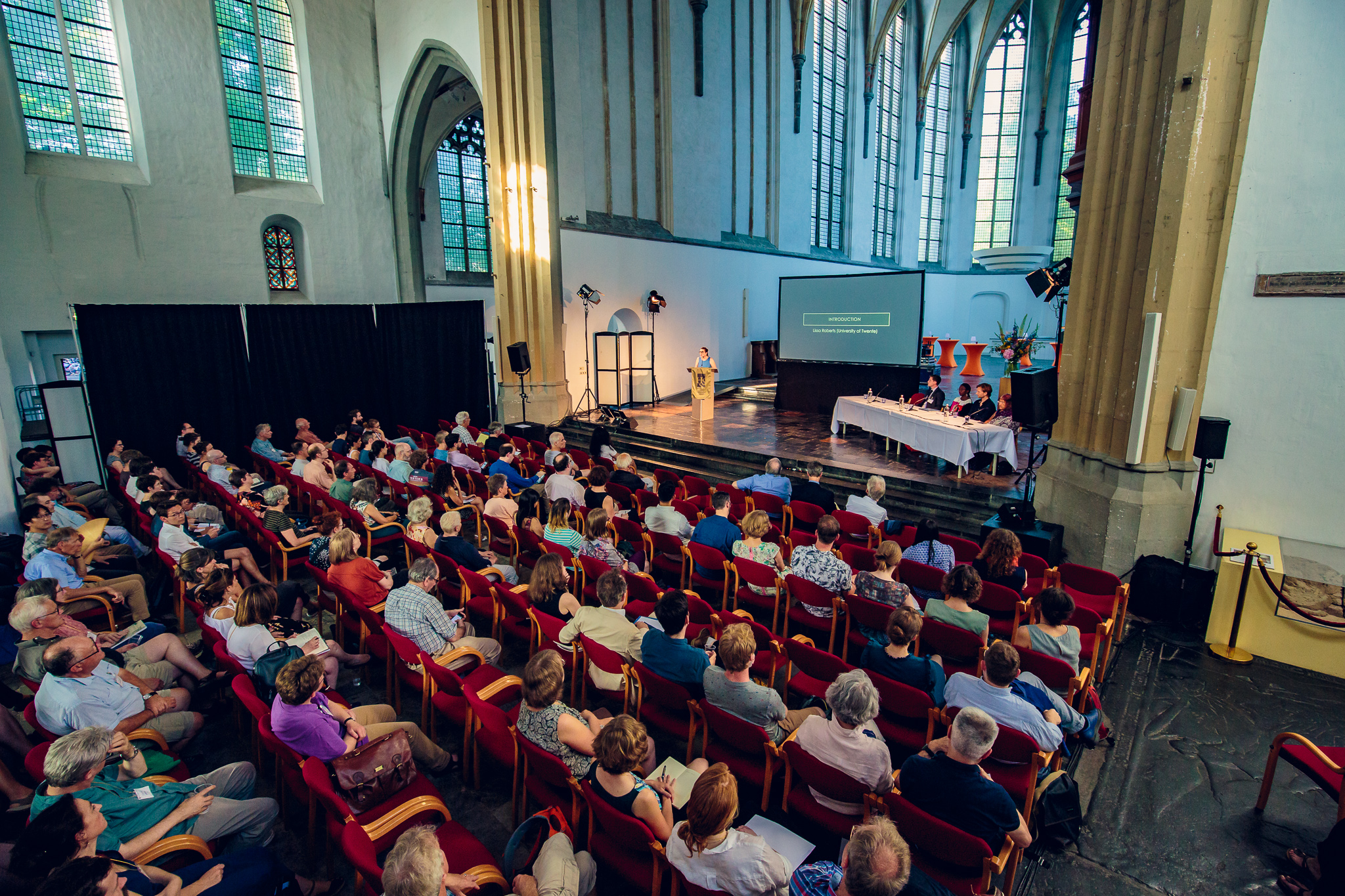 Conference meeting with dozens of people seated and looking at a presentation in a church-like setting