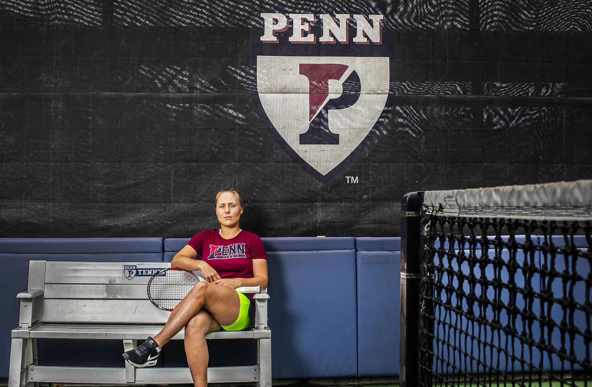 Bryzgalova sits on a bench at the Penn tennis courts, holding her racquet.