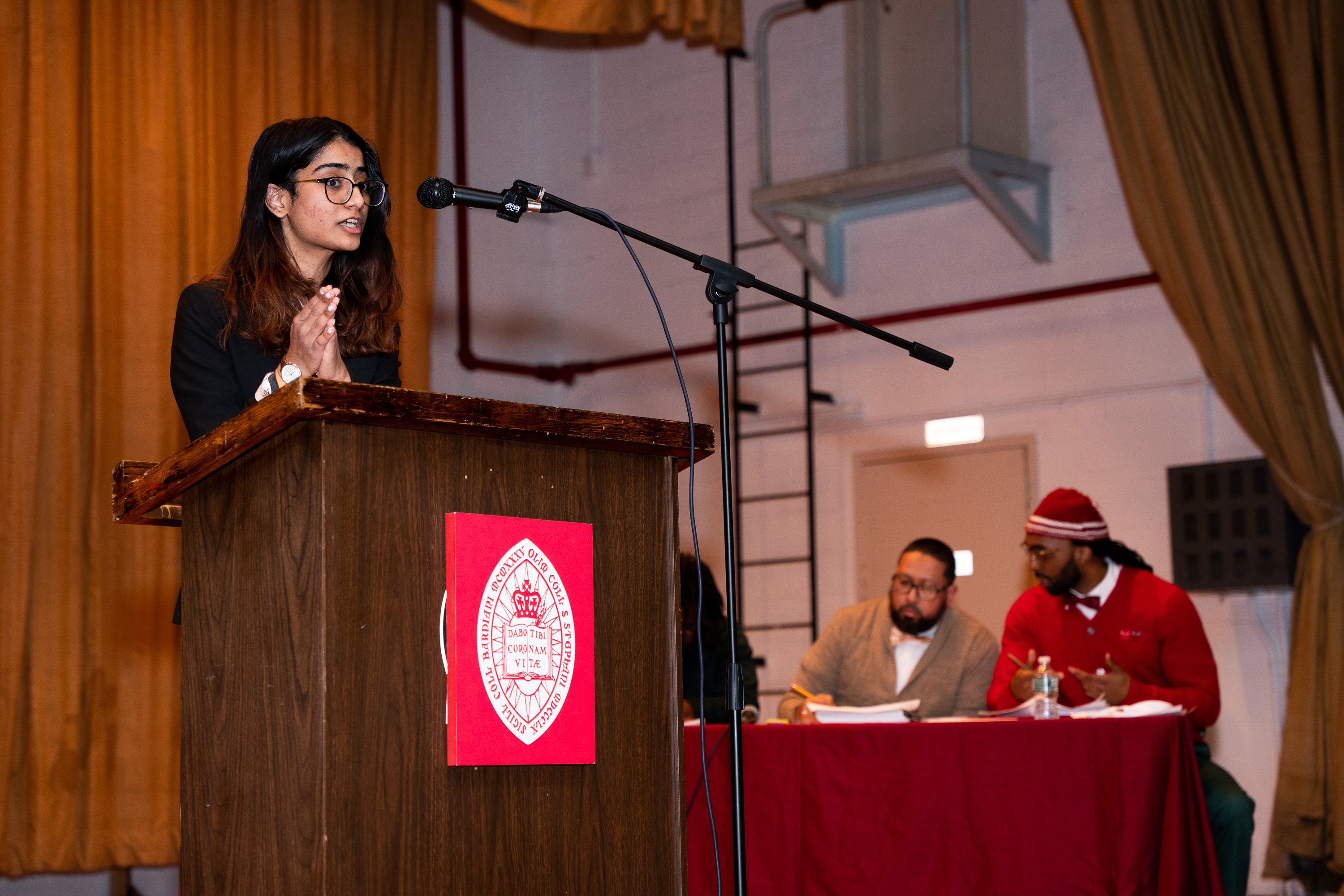 Penn debate student speaks at podium as members of the Bard Prison initiative are seen at a table to her left