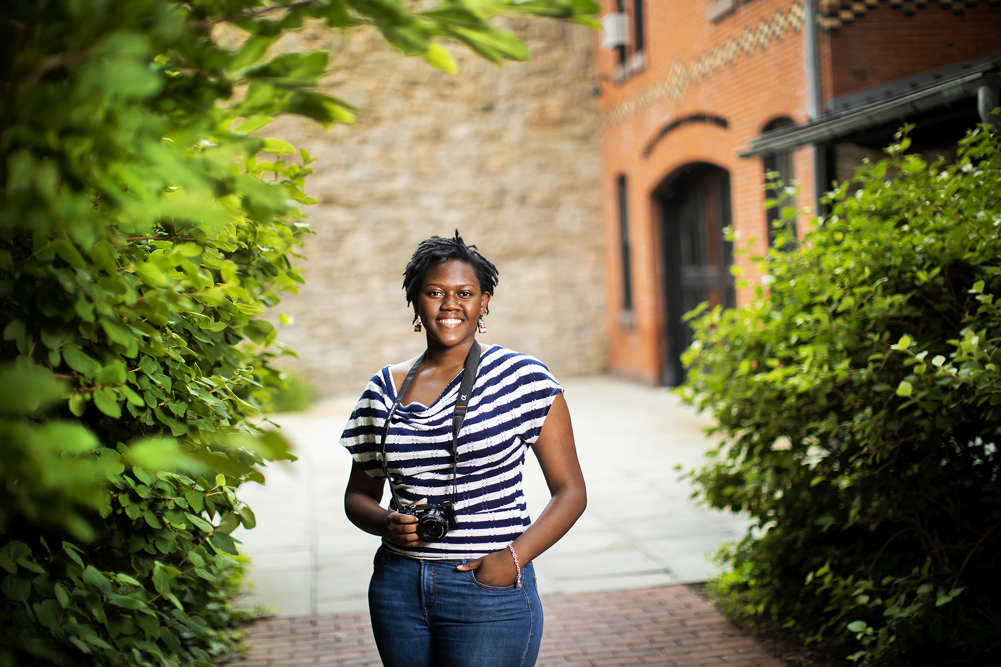 Tamia Harvey-Martin smiles in front of the LGBT Center with one hand in her pocket and one hand on a camera hung on a strap around her neck