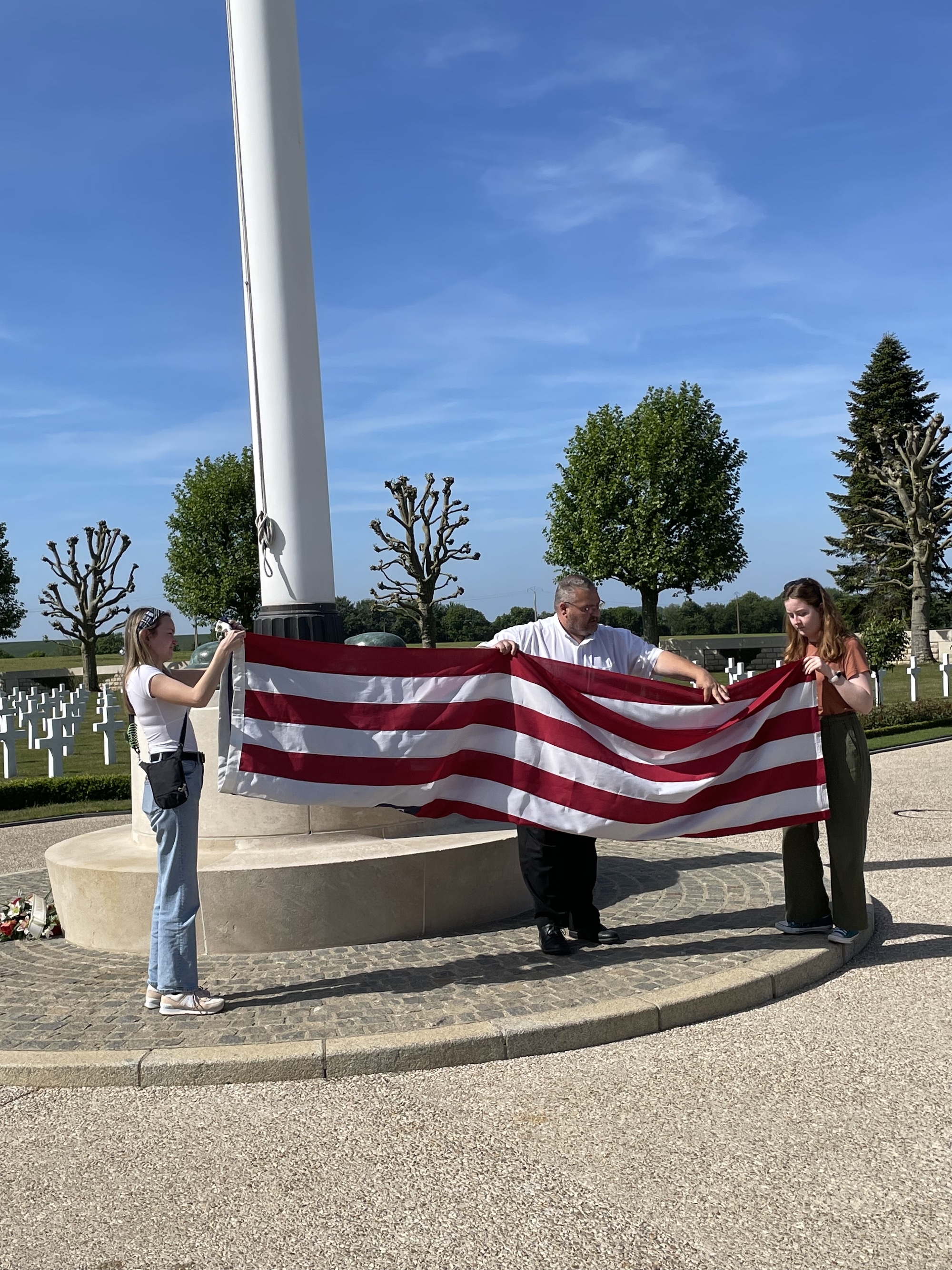 Two students help a French caretaker of an American cemetery in France fold the U.S. flag.