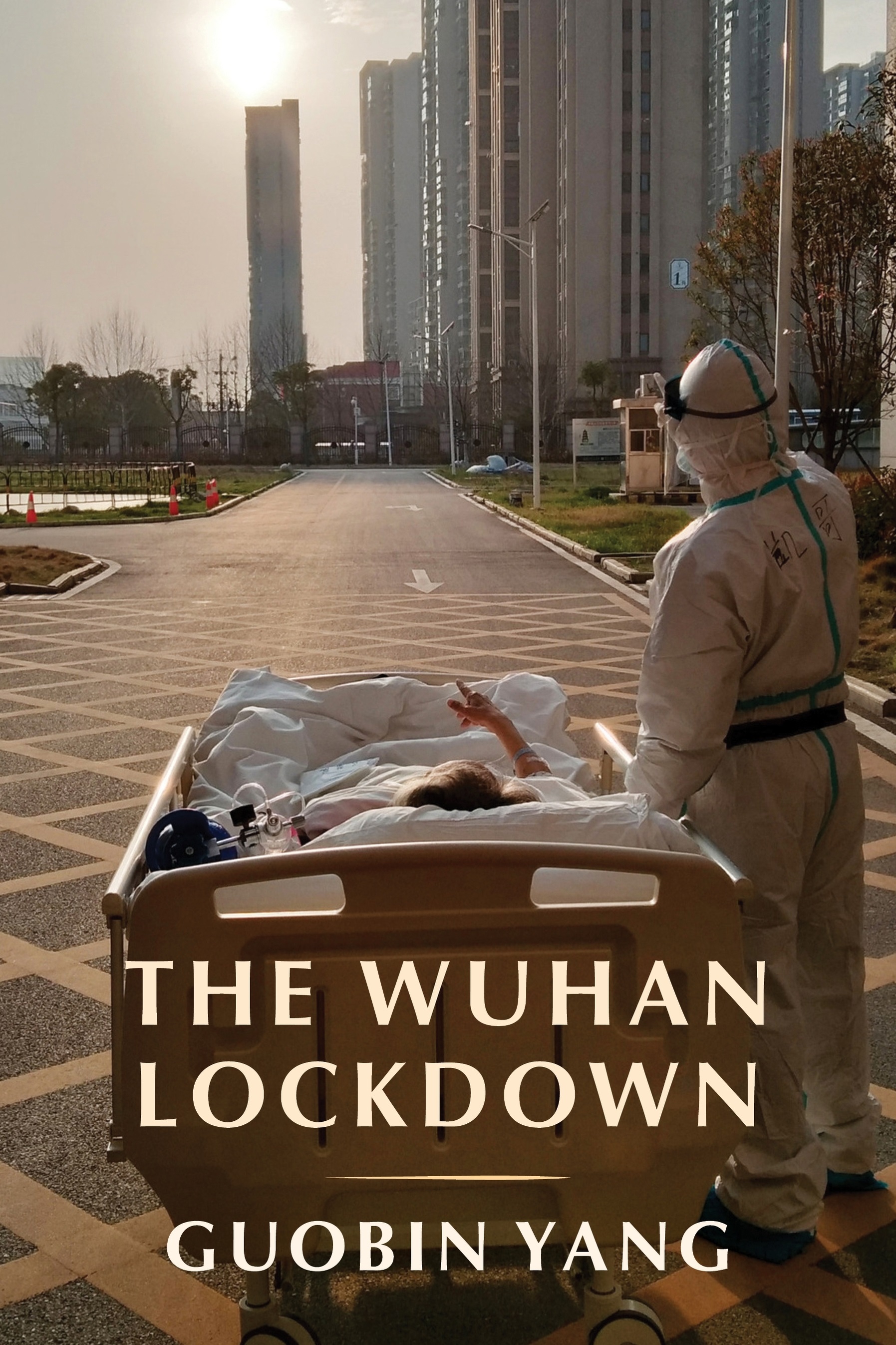 Cover of the book called "The Wuhan Lockdown by Guobin Yang." The image shows a person fully covered in what appears like a hazmat suit next to a person in a hospital bed. They are outside.
