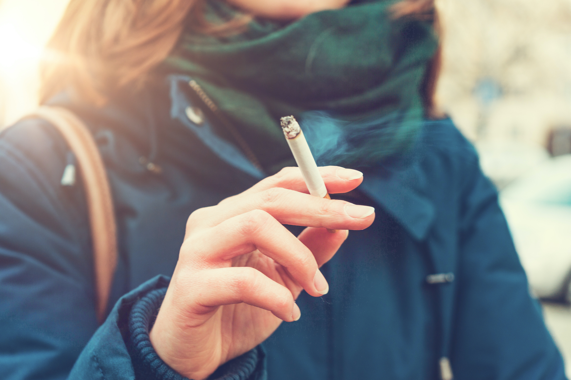 A hand holding a cigarette with just the torso of the person showing in the background.