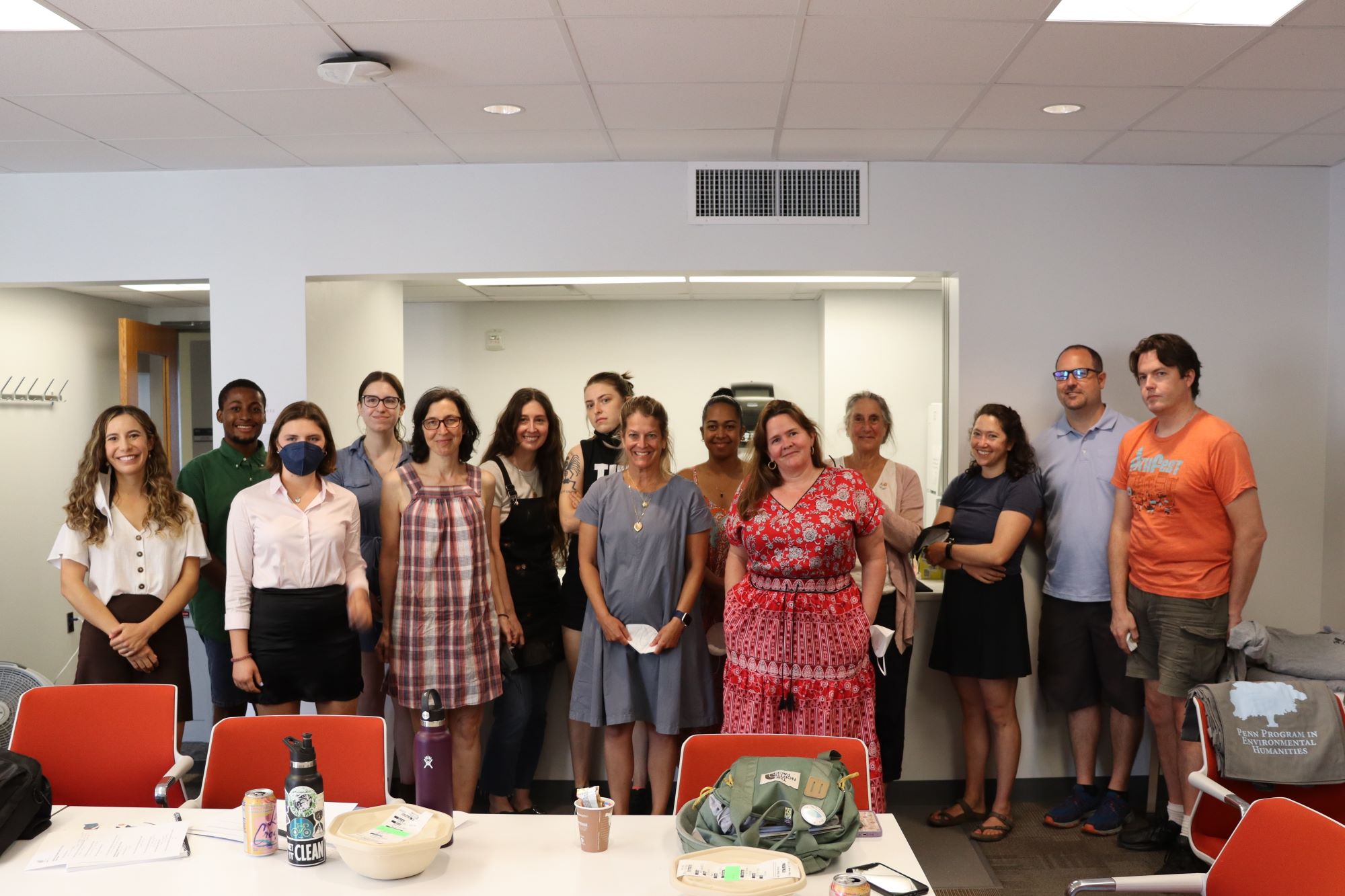 A group of 13 people stand in a classroom smiling.