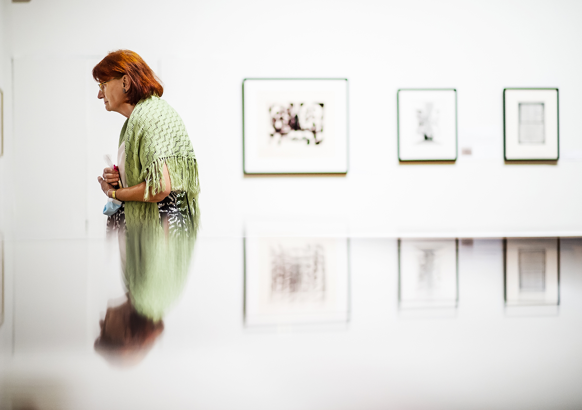 A person walks past three artworks hanging on the wall at the Arthur Ross Gallery.