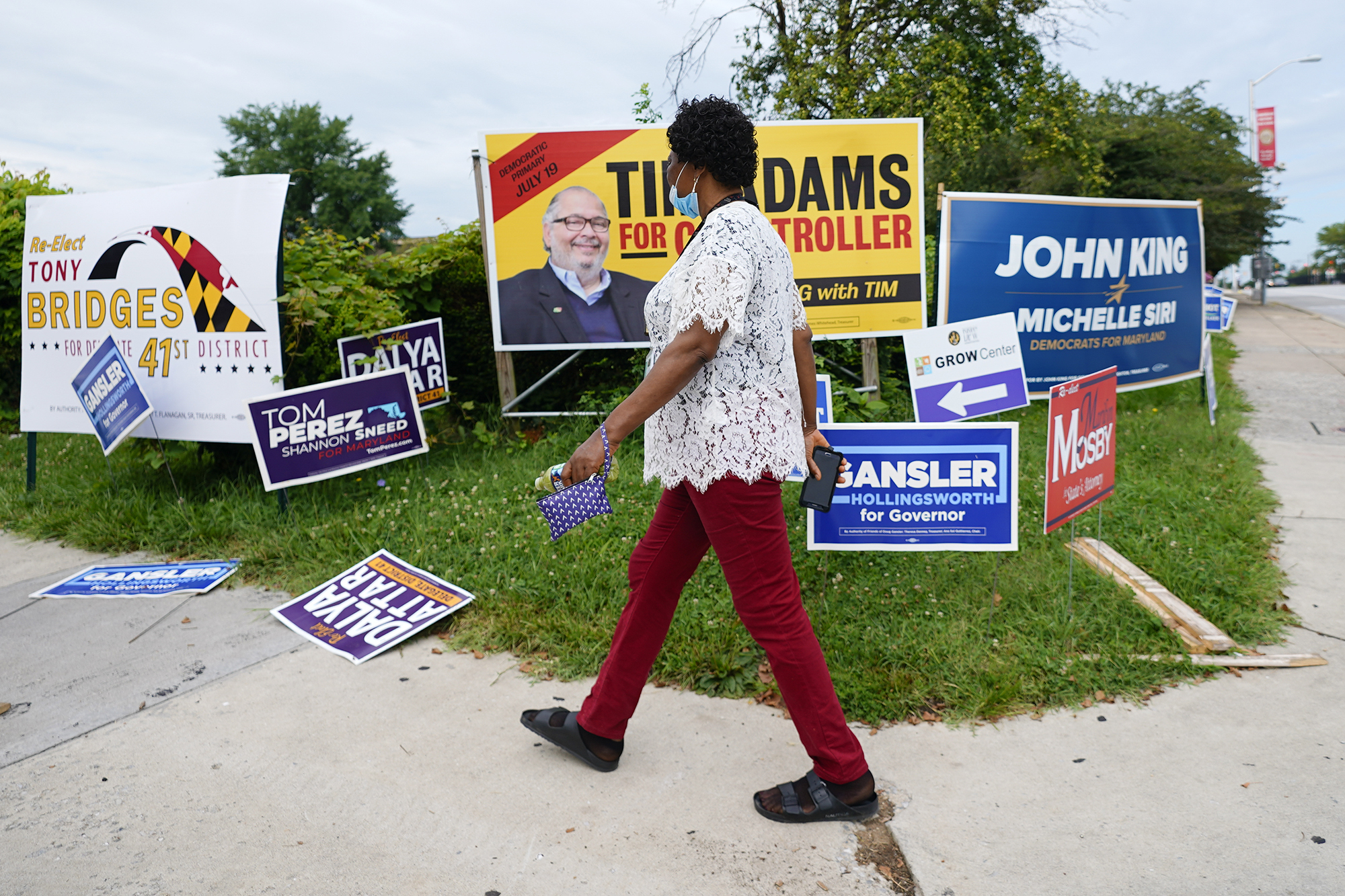 Woman wearing face mask walks along sidewalk lined with campaign signs