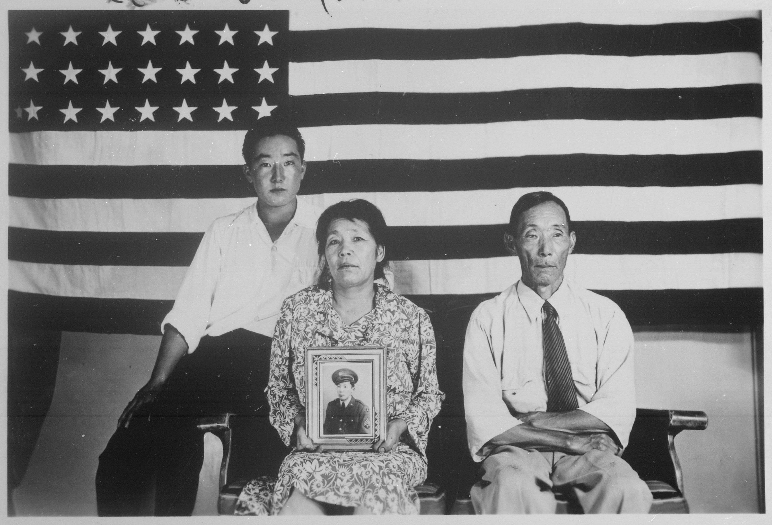 Japanese Americans posing in front of American flag with a photo of a serviceman being held