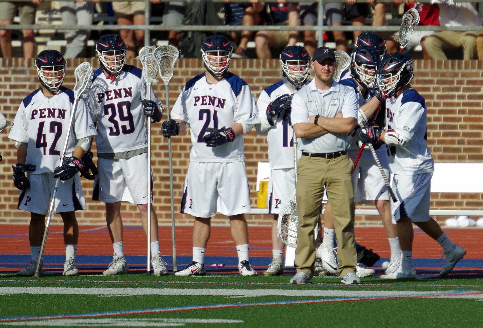 Anthony Erz, at right with arms crossed, observes play on the field with members of the lacrosse team.