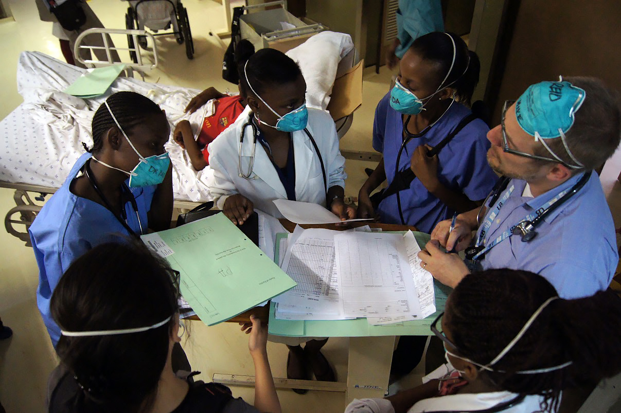 Six medical people in scrubs and masks discussing medical charts in Botswana.