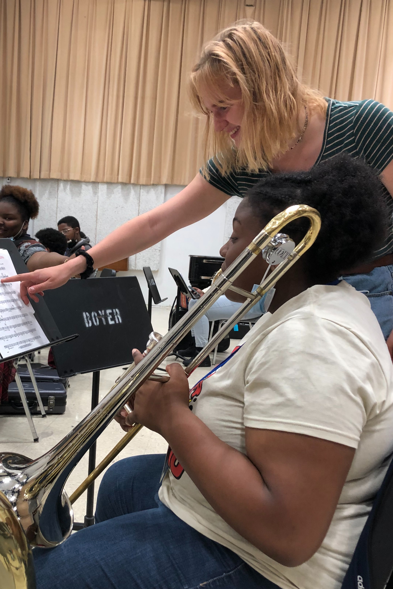 Chaily Deresckey points to music on a stand while helping student playing trombone, 