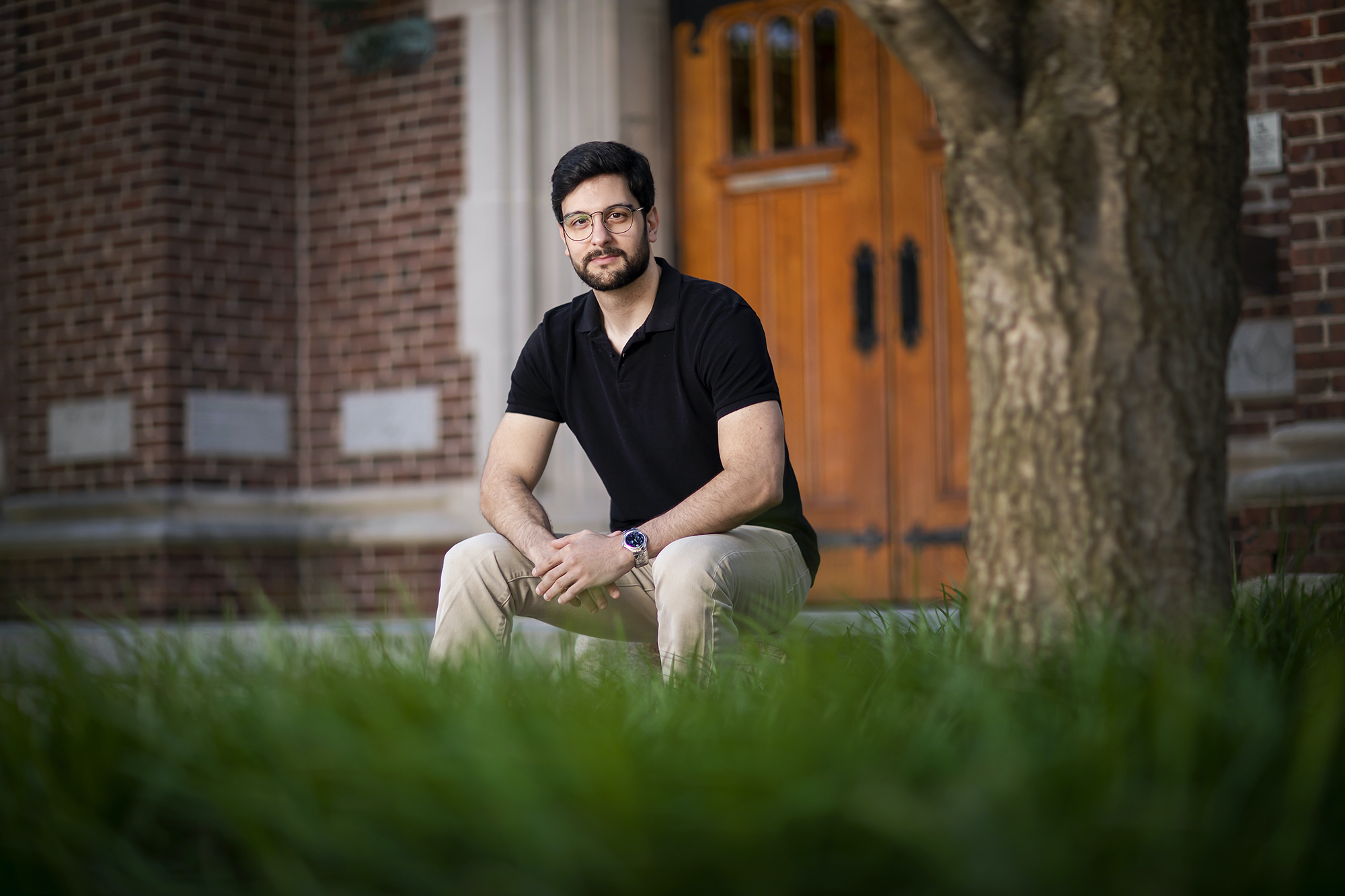 Ibrahim Bakri sits on a bench in front of wooden double doors and a red brick building