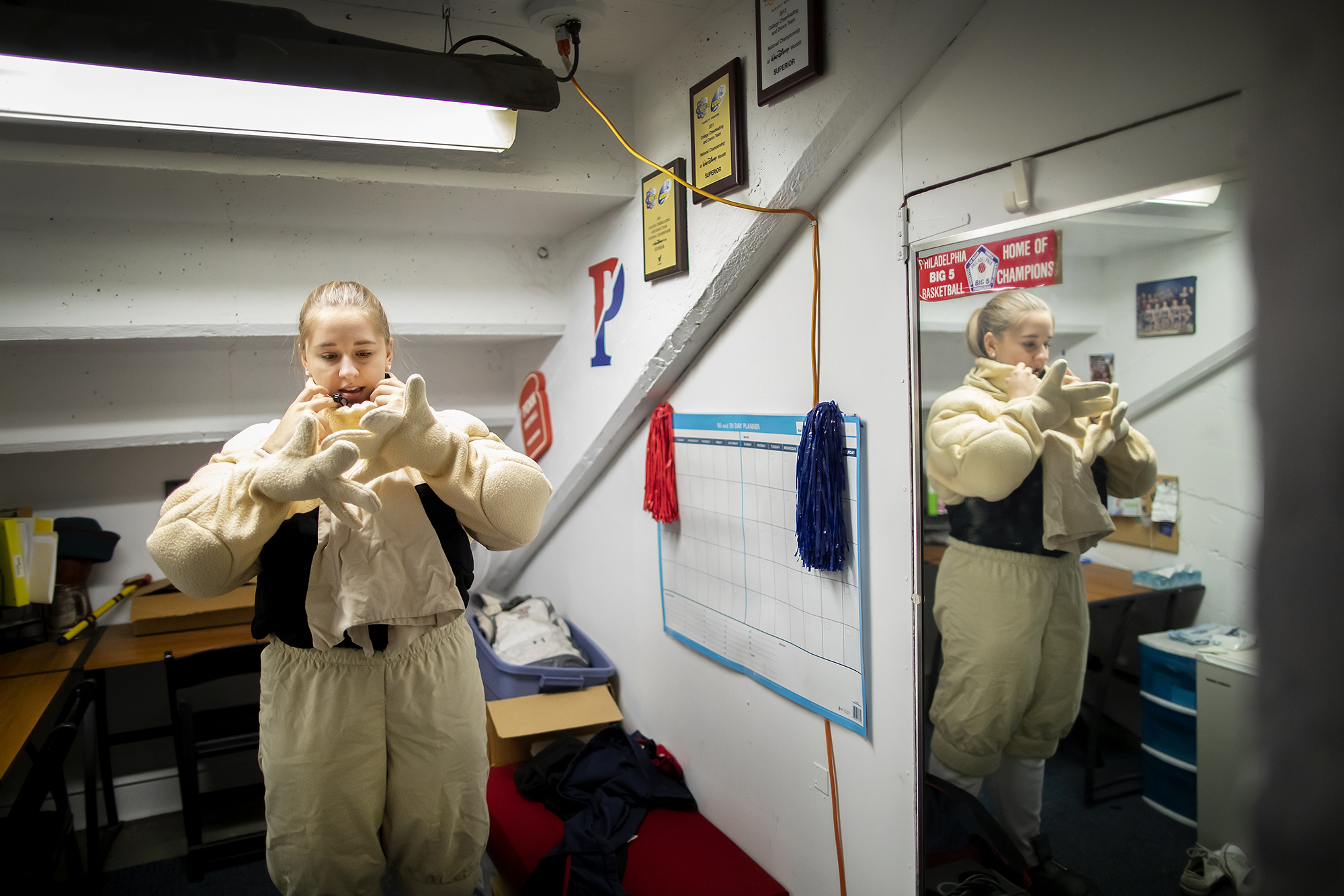 Sophia Zehler puts on the Penn Quaker mascot gloves in a changing room in the Palestra.