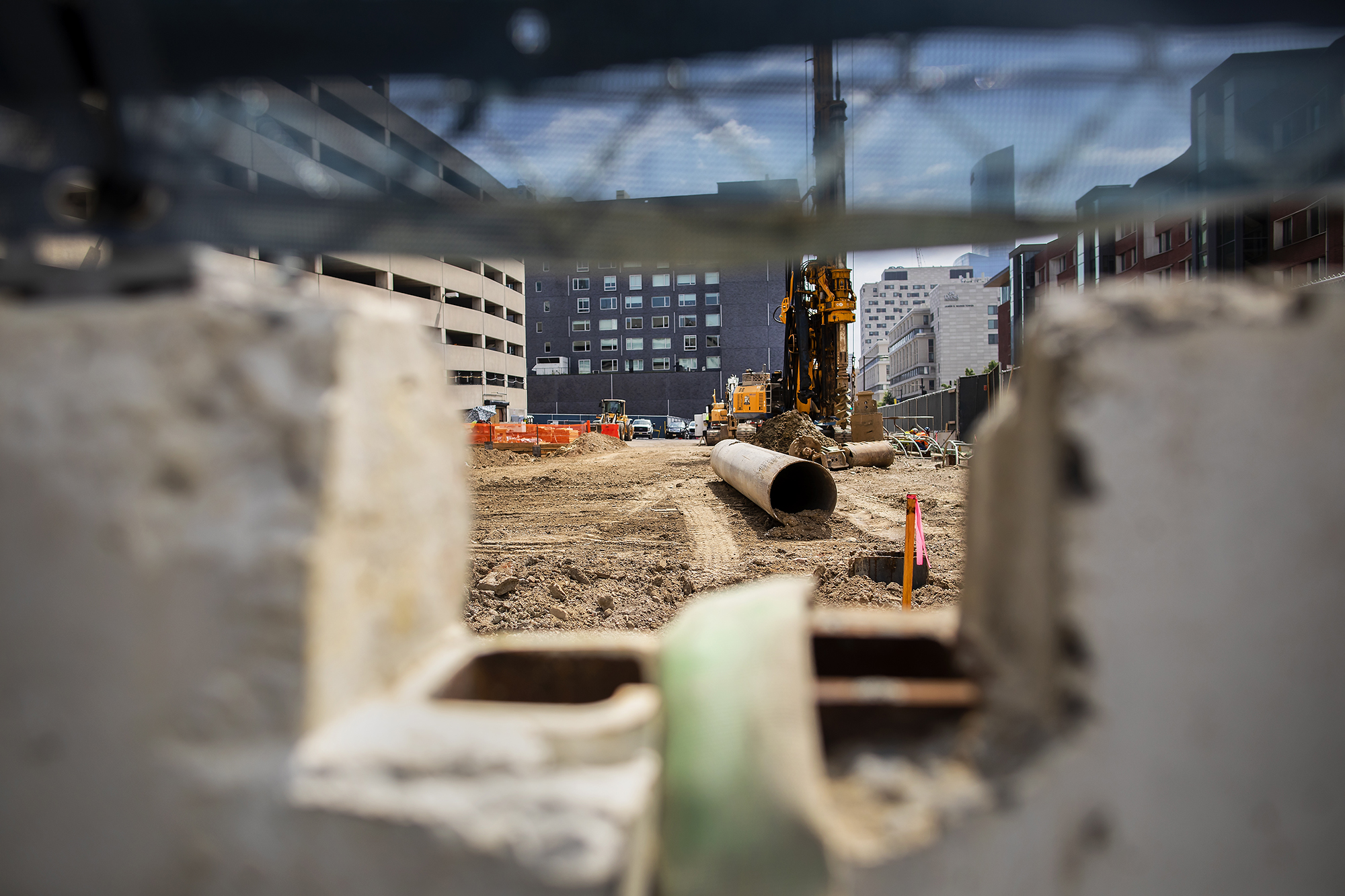 View through a hole in a concrete wall of a razed dirt area with construction equipment on Penn’s campus.