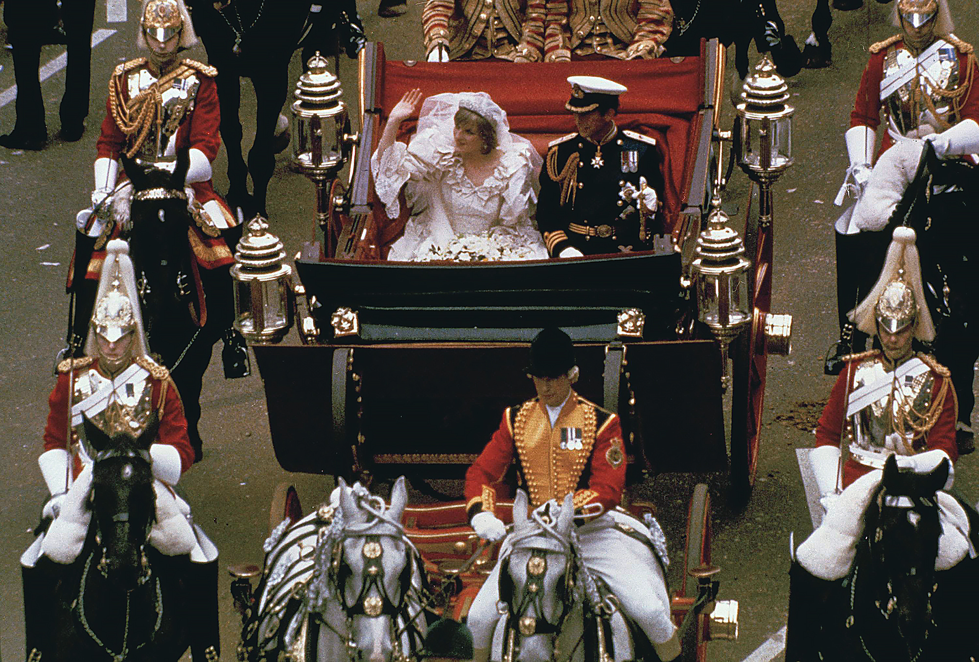 Princess Diana, waving to the crowds, and Prince Charles in an open, horse-drawn carriage on their wedding day