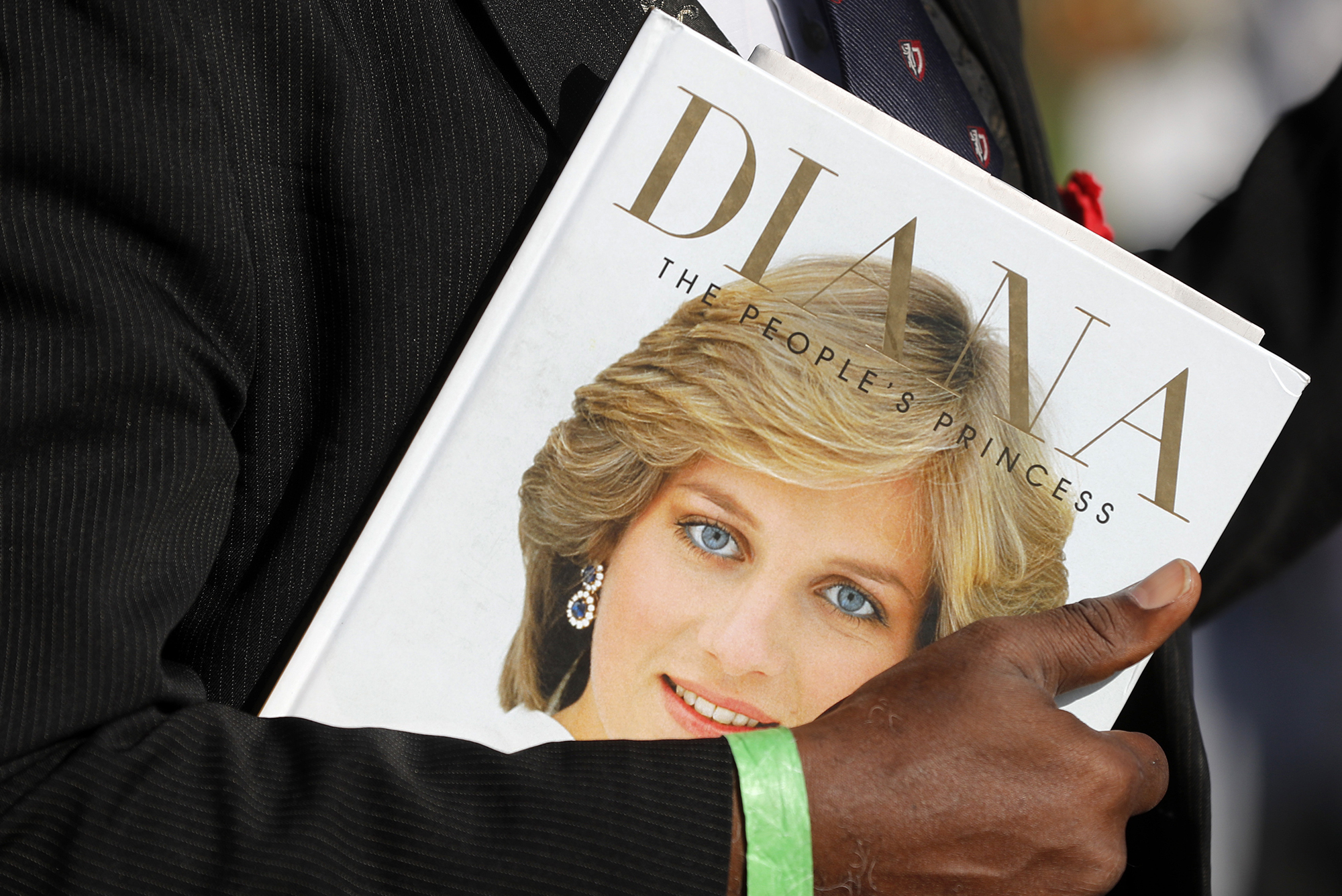 A book entitled "Diana, the People's Princess" with a photo of her face is being held by a man in a suit