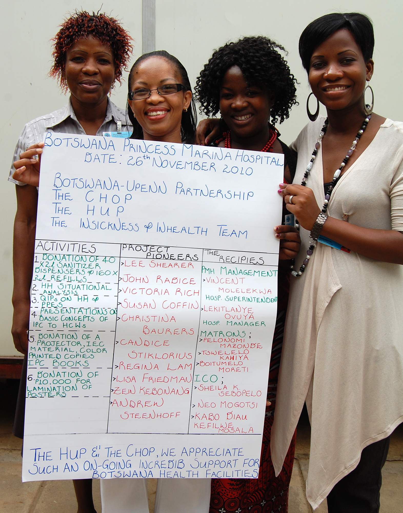 Four people standing holding a large sign with handwritten information about Upenn-Botswana program.