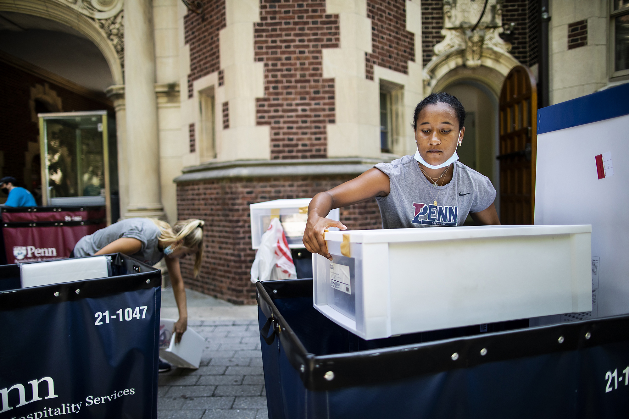 A person pulls a plastic bin out of a moving bin in front of one of Penn’s College Houses.