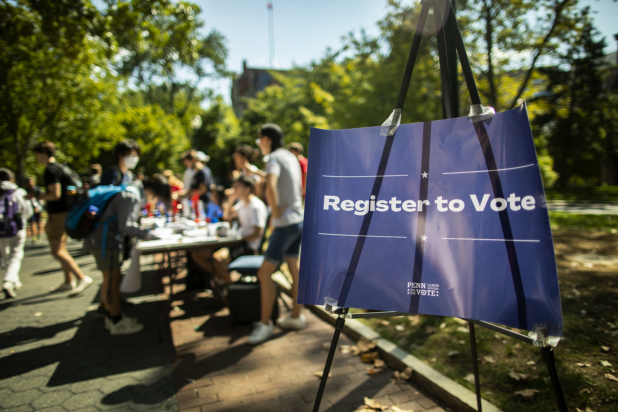 A sign on Locust walk next to tables and students reads Register to Vote.