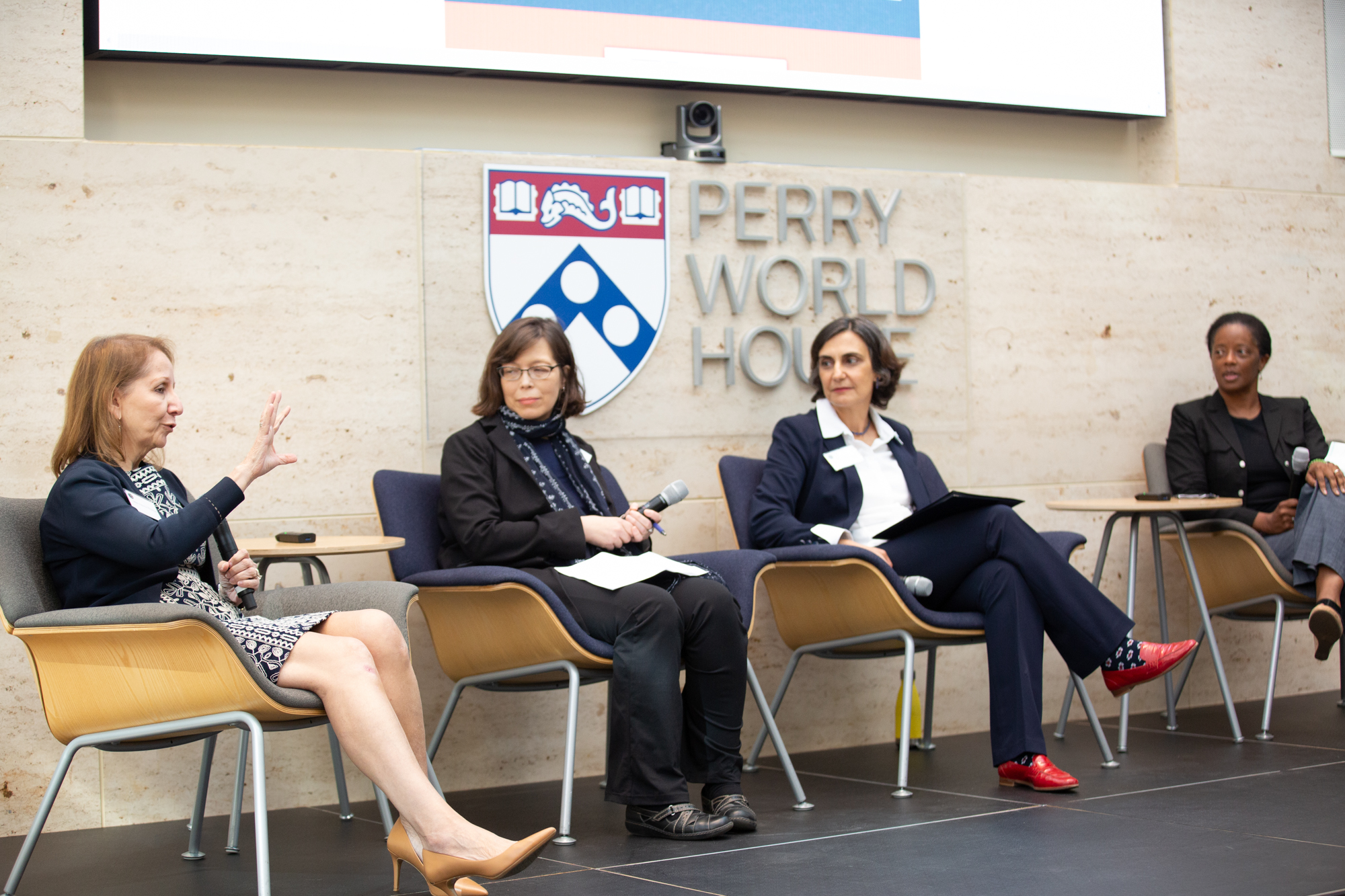 Antonia M. Villarruel addresses the audience while Emily Hannum, Tulia Falleti, and LaShawn Jefferson look on. A sign behind the group reads: Perry World House. 