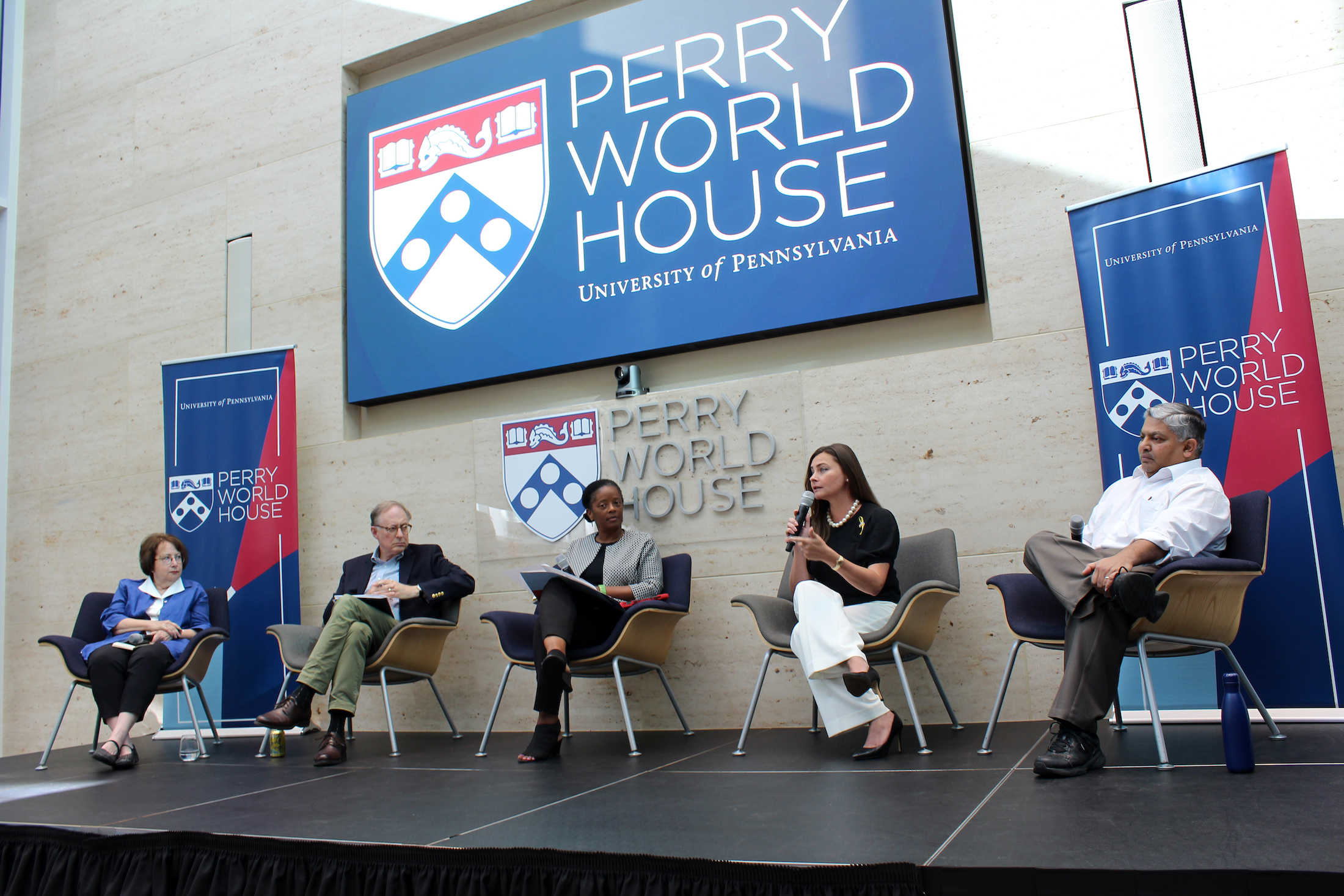 Five people sit in chairs on a stage at Perry World House