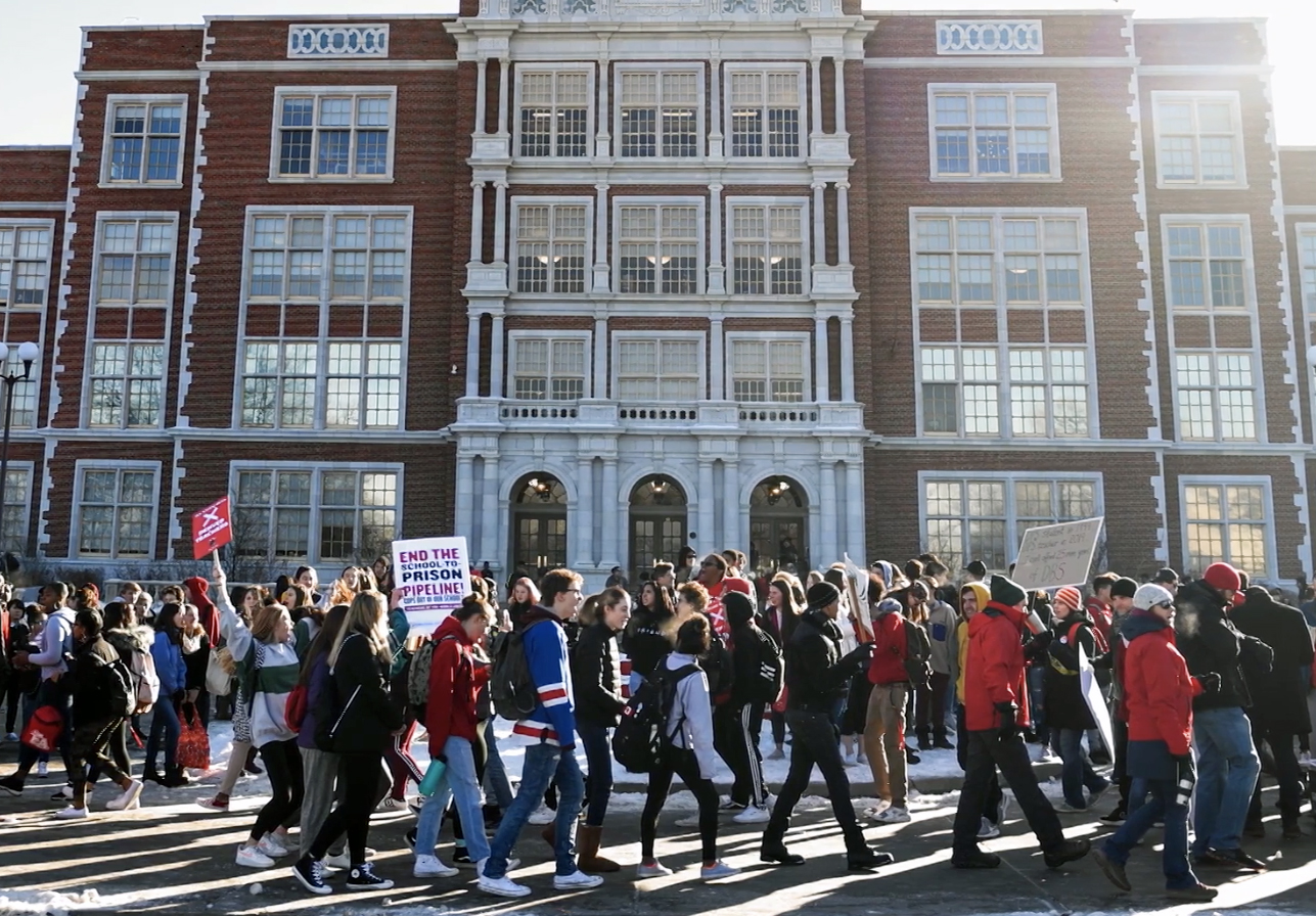 A group of students demonstrating in front of a school building.