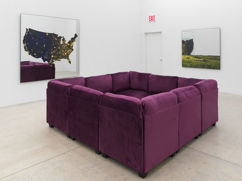 An exhibition by Ken Lum of a purple couch with four sides and two prints hanging on the wall.