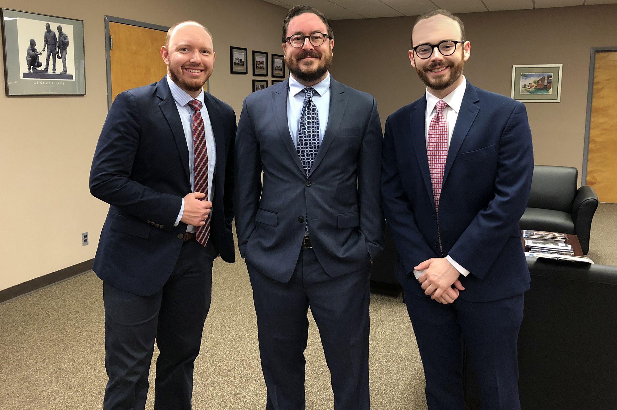 Three men in suits pose together in an office