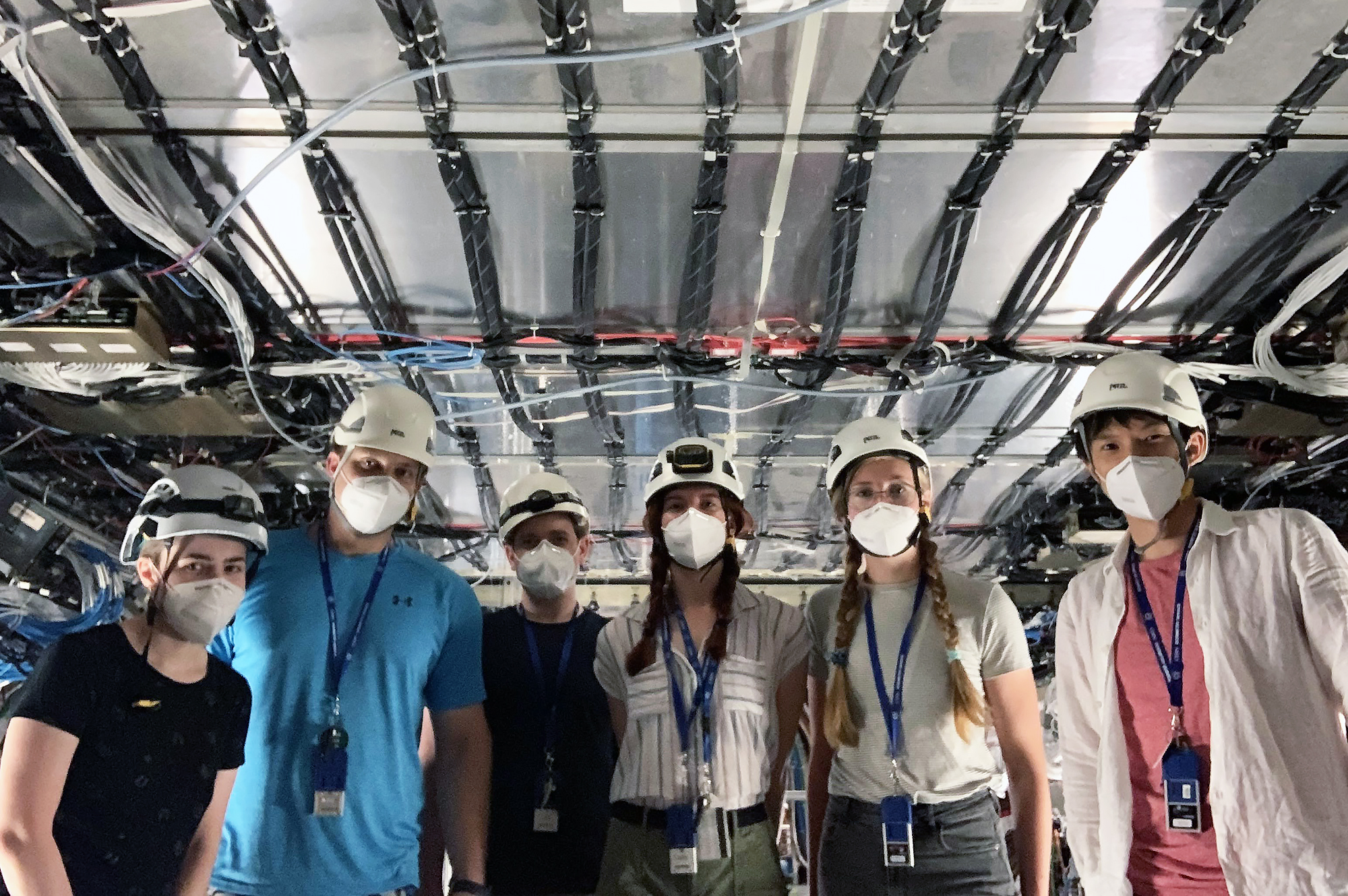Six masked people wearing helmets inside the particle accelerator.