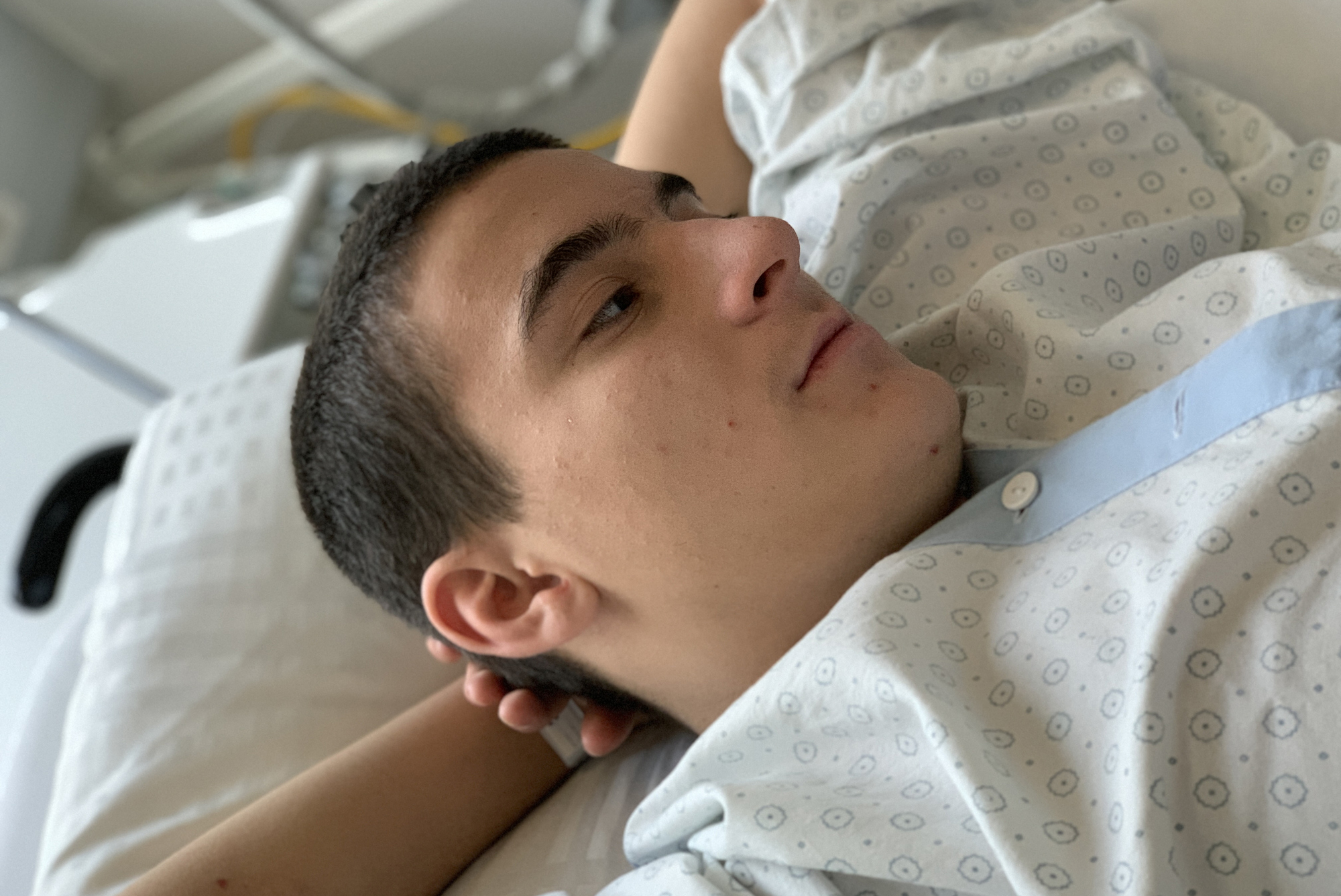 A teenager lying on their back in a hospital bed.