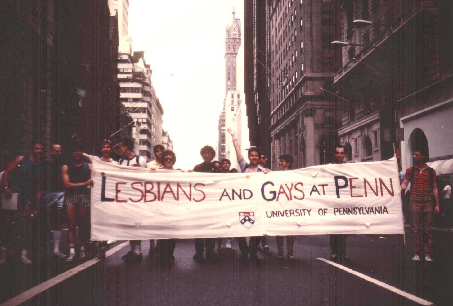 A group of people striding through Center City, Philadelphia carrying a banner that says "Lesbians and Gays at Penn"