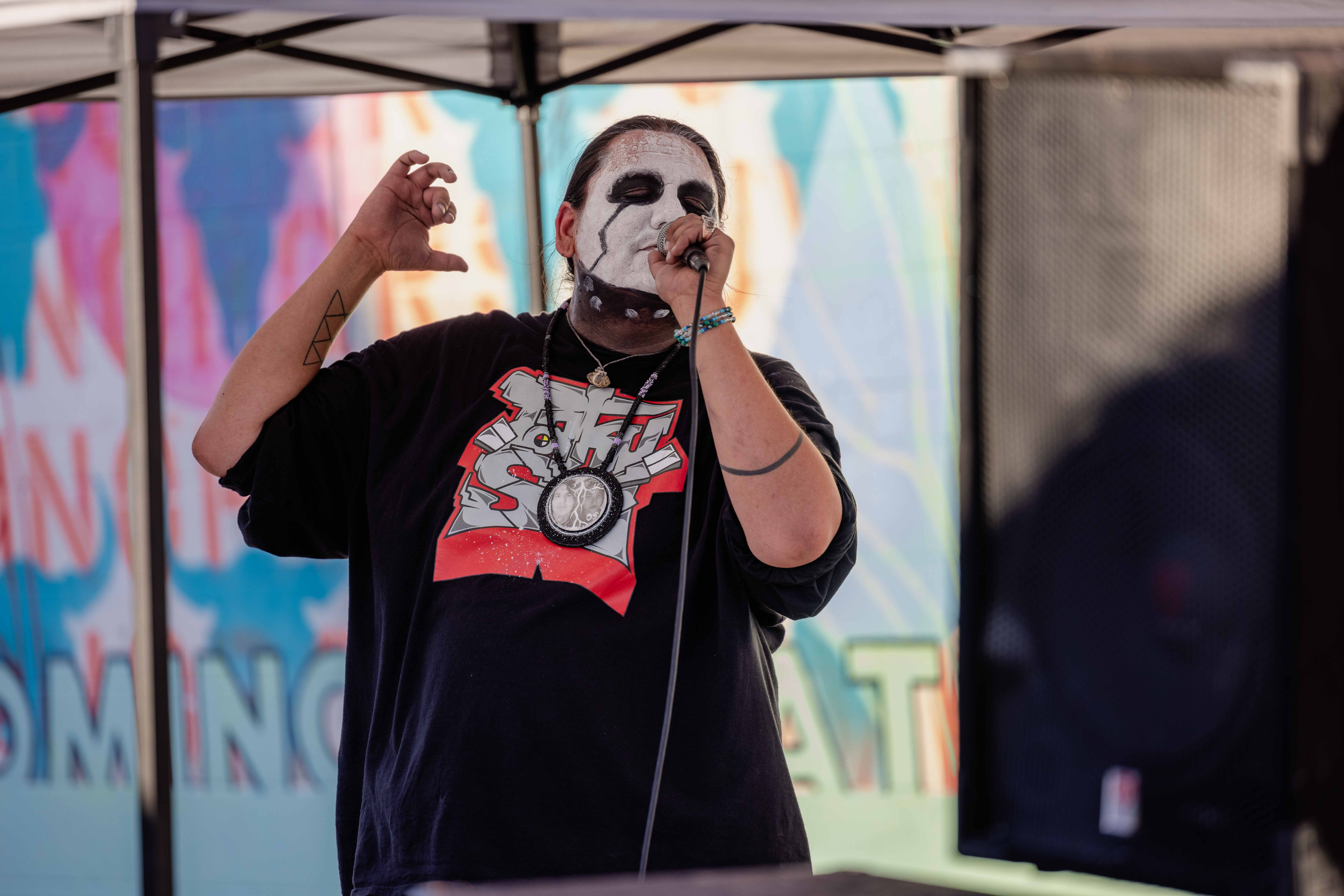 Person with painted face sings with closed eyes into a microphone