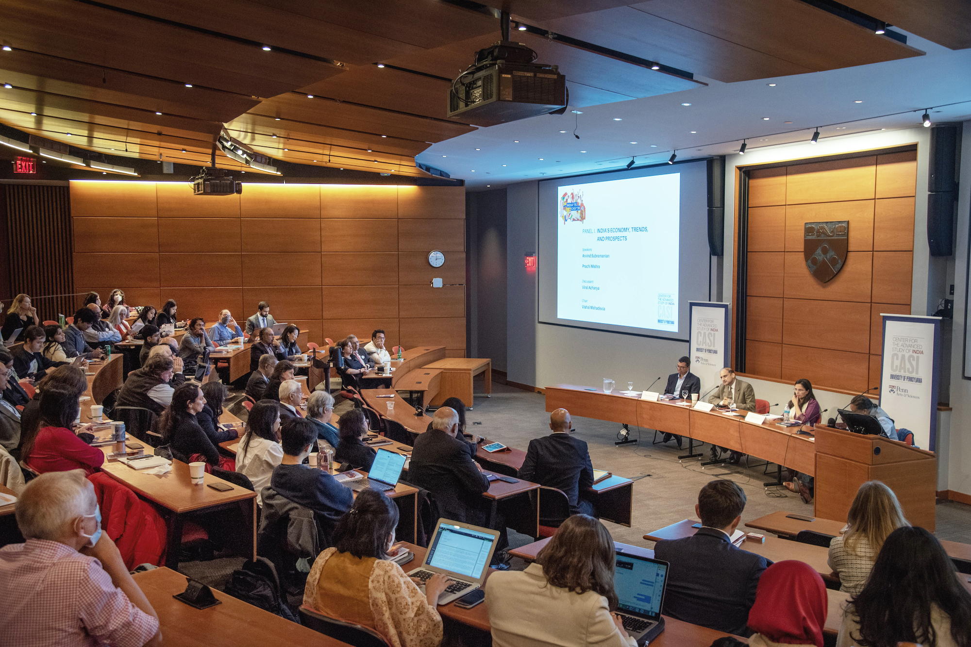 A room full of people listening to a panel of presenters