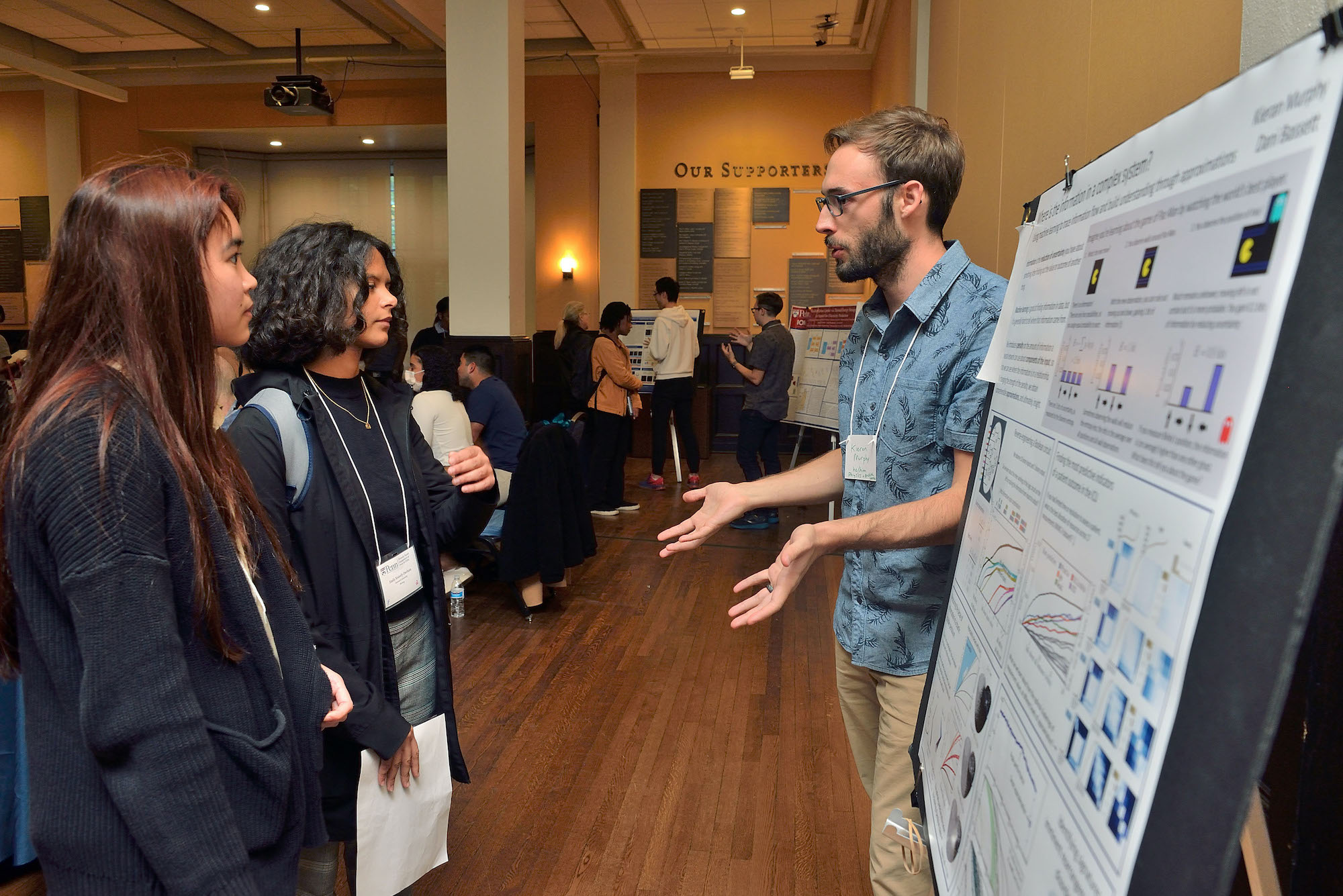 Student talks to two others while standing beside a research poster