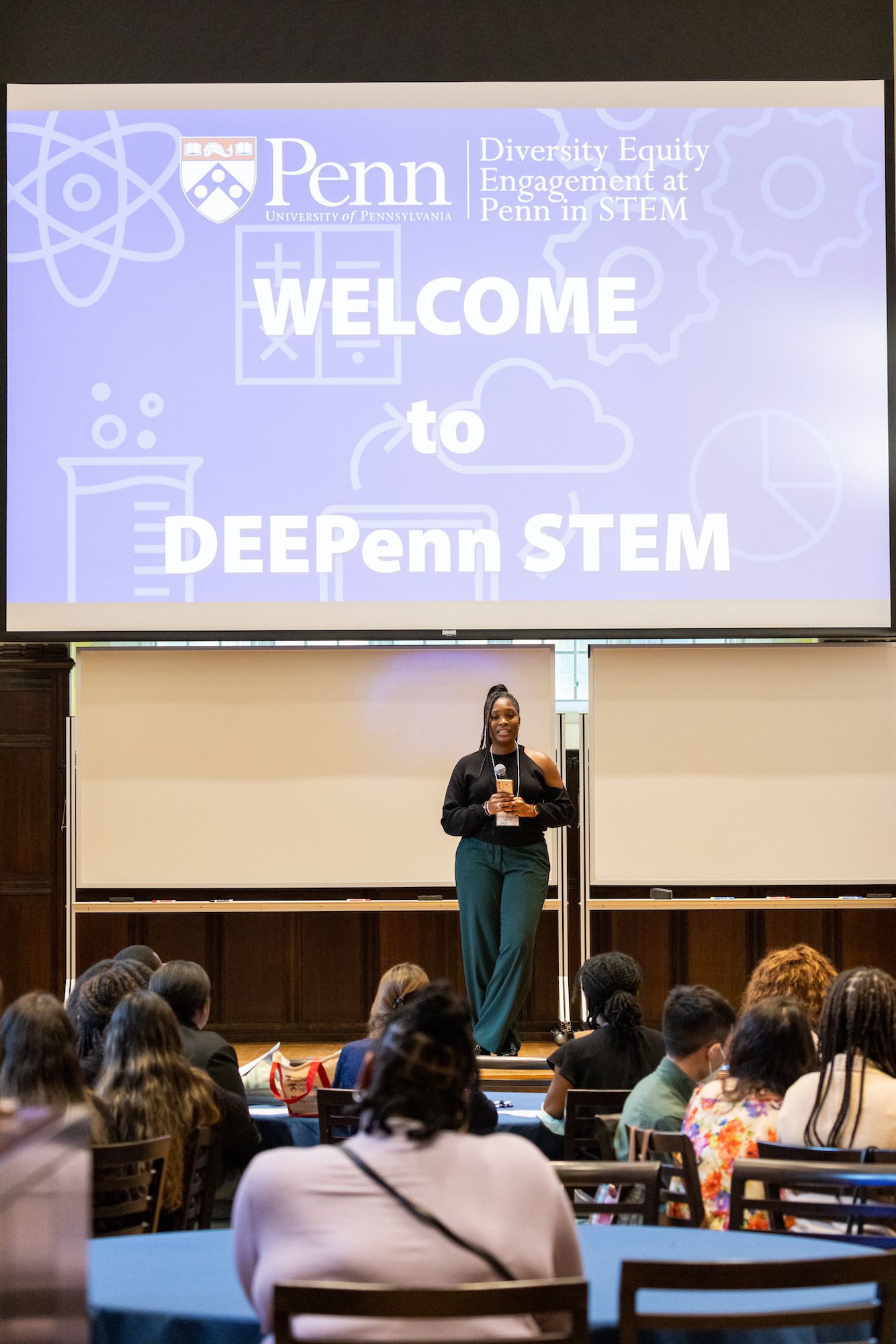 Ashley Wallace stands on a stage in front of scree that says Welcome to DEEPenn STEM